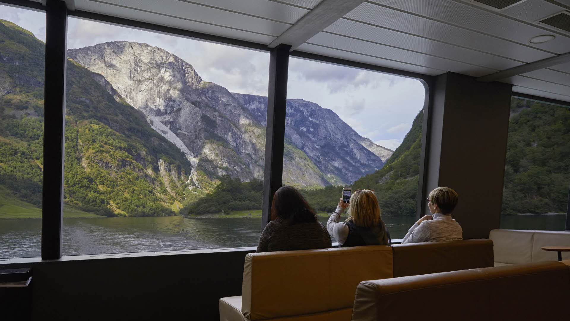 Trois amies prennent des photos du paysage du Nærøyfjord à travers les grandes baies vitrées panoramiques du Future of The Fjords.