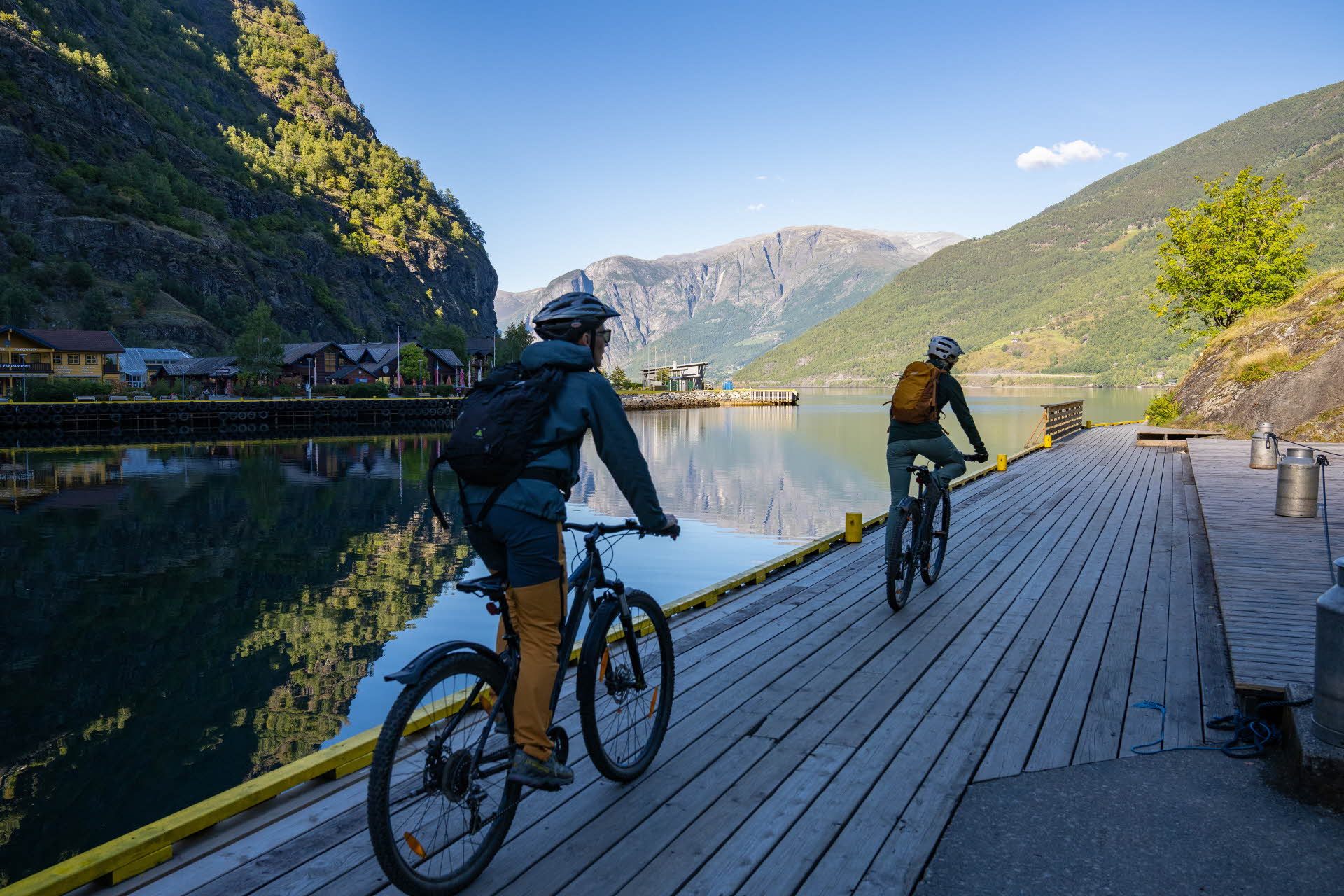 Two cyclists on the quay in Flåm with views of the sunny fjord.