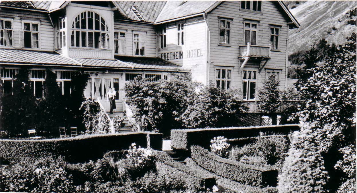 Photo en noir et blanc du Fretheim Hotel avant 1900. Une personne sur les escaliers du hall, avec le jardin en avant-plan.