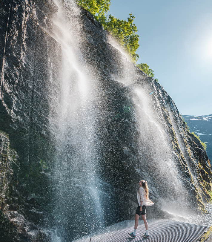 A woman standing under a shower from a waterfall in Geiranger.