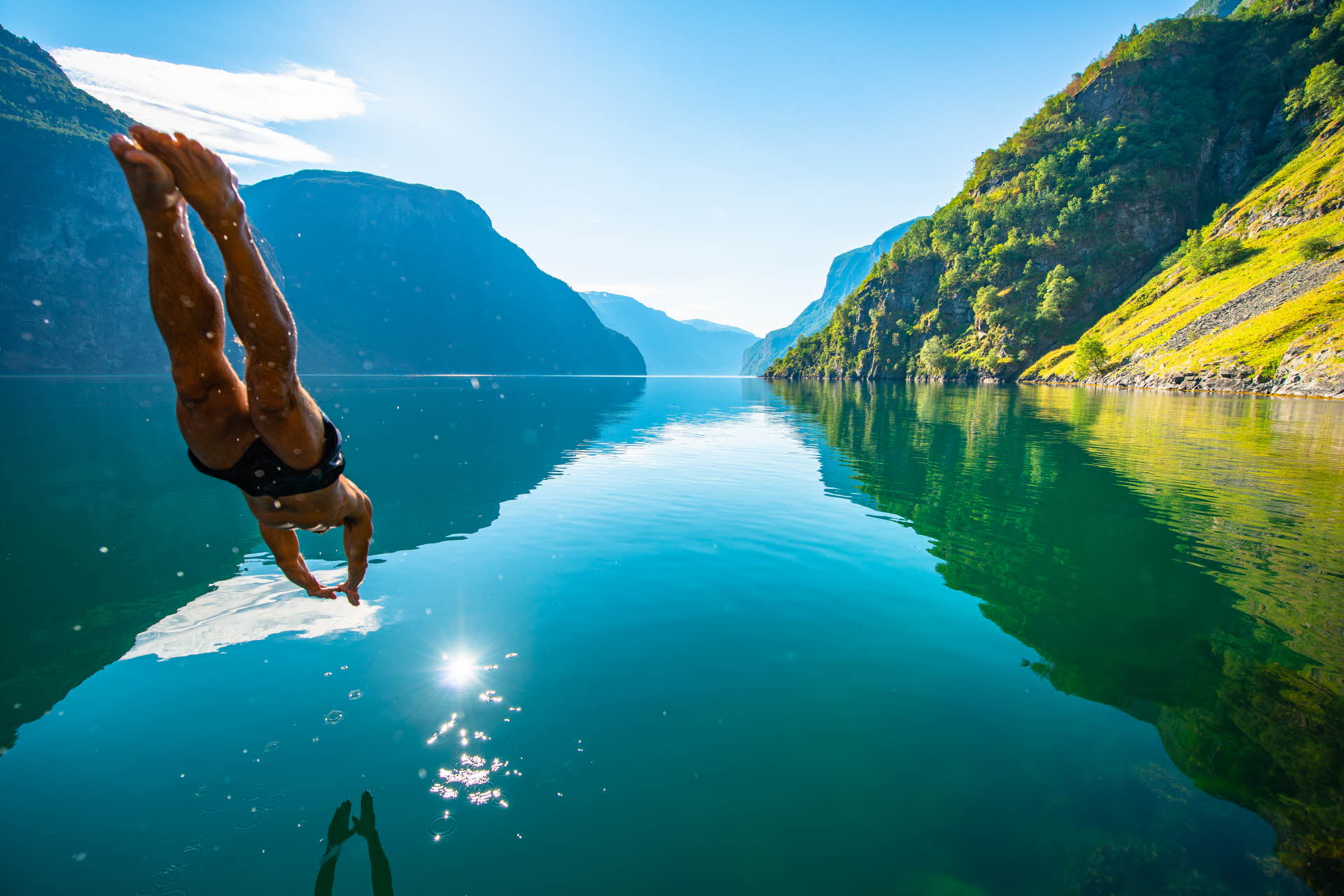 Ein Mann taucht im Sommer in den ruhig daliegenden Nærøyfjord ein