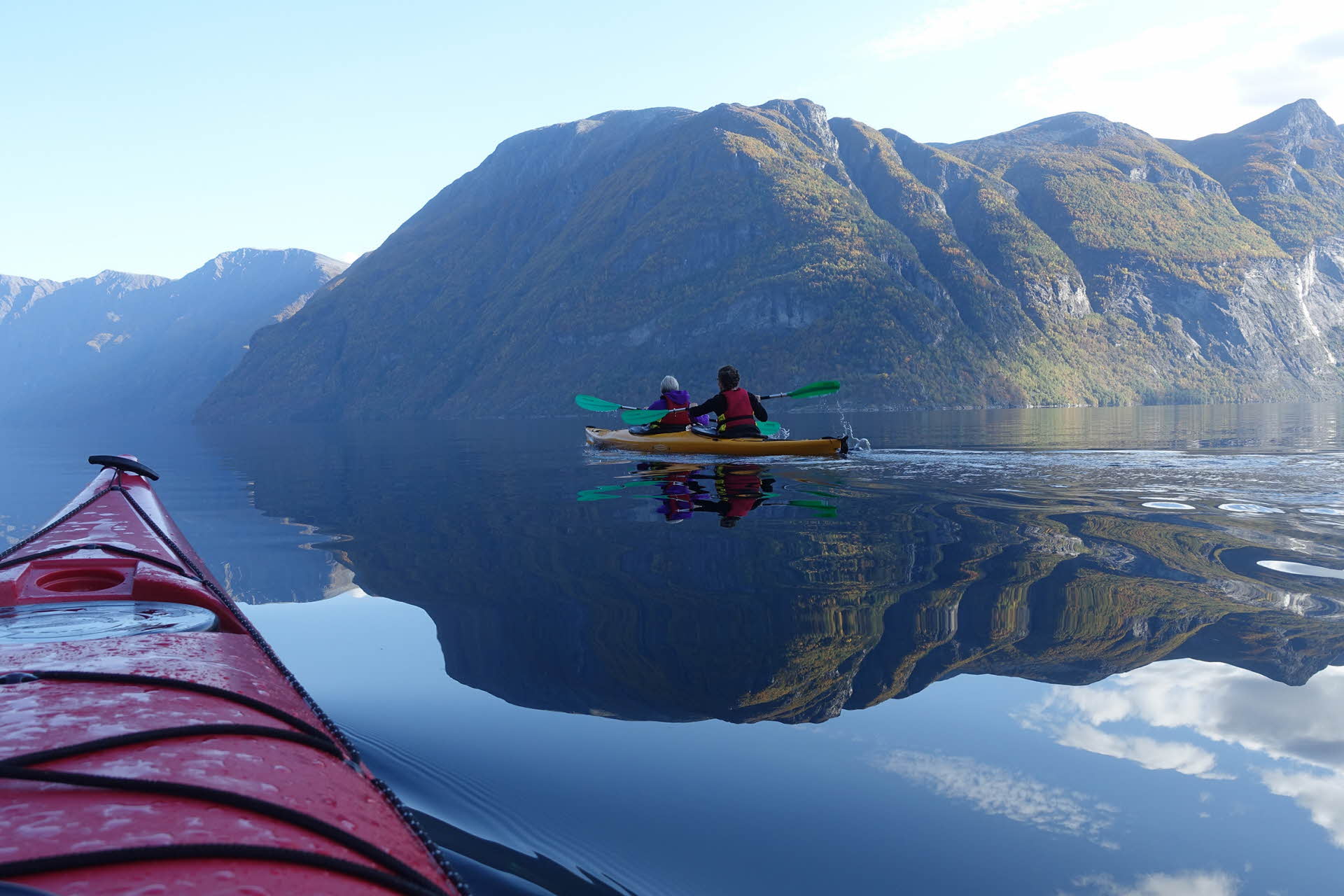 Zwei Personen in einem gelben Kajak paddeln in Geiranger durch den ruhig daliegenden Fjord