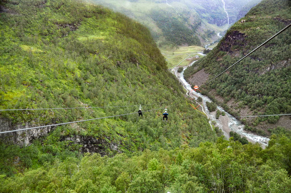 Two people hanging from the Flåm Zipline on their way down towards Flåmsdalen