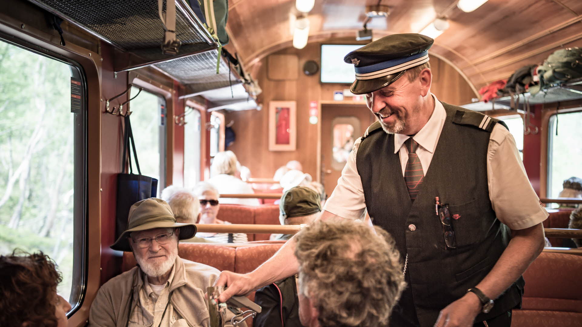 Ein lächelnder Schaffner kontrolliert die Fahrkarten dreier Touristen in der Flåmbahn