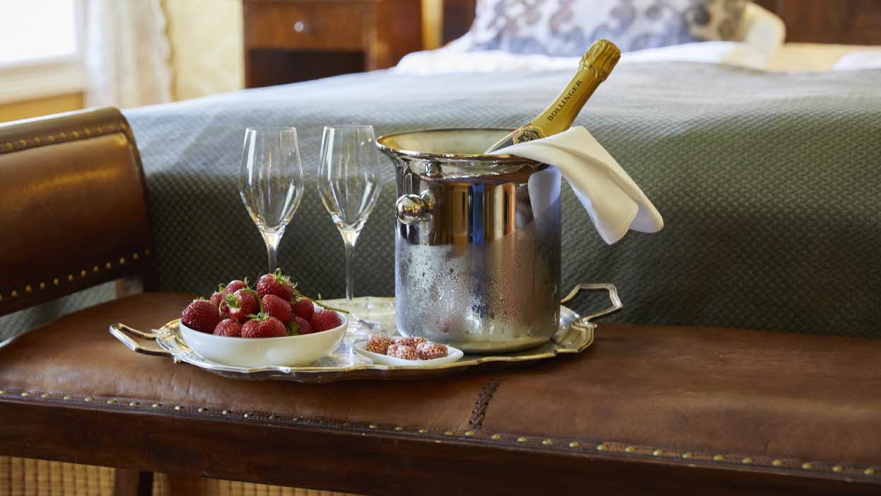 Un plateau avec une bouteille de champagne dans un seau, deux flûtes et des fraises, posé à côté d’un lit dans l’une des chambres historiques du Fretheim Hotel