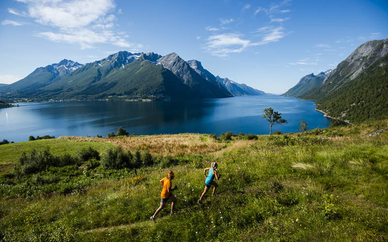 A man and a woman running on a trail above the Hjørundfjord