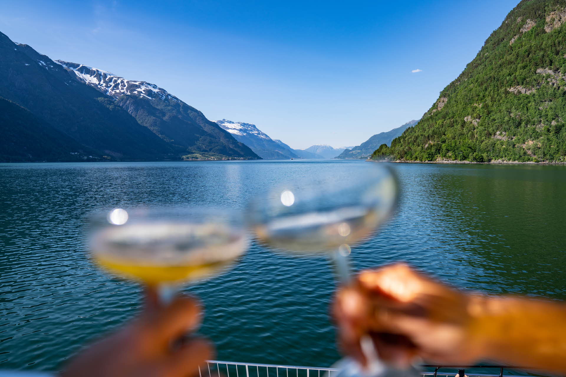 Two hands holding champagne glasses making a toast with cider on the Hardangerfjord