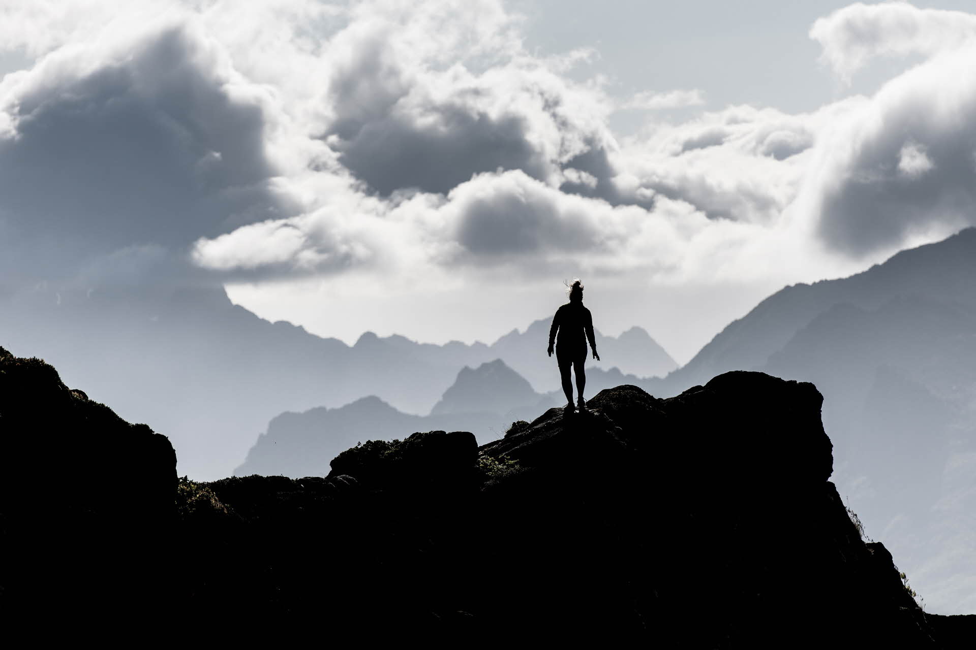 En person går på en steinklippe. Flere fjell i horisonten og dramatiske skyer over.