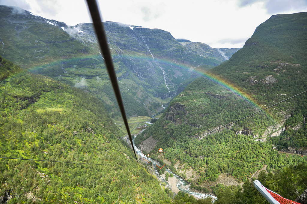 View from start platform Flåm Zipline. Rainbow is going across the deep and steep Flam valley. Green icy river flow down in valley