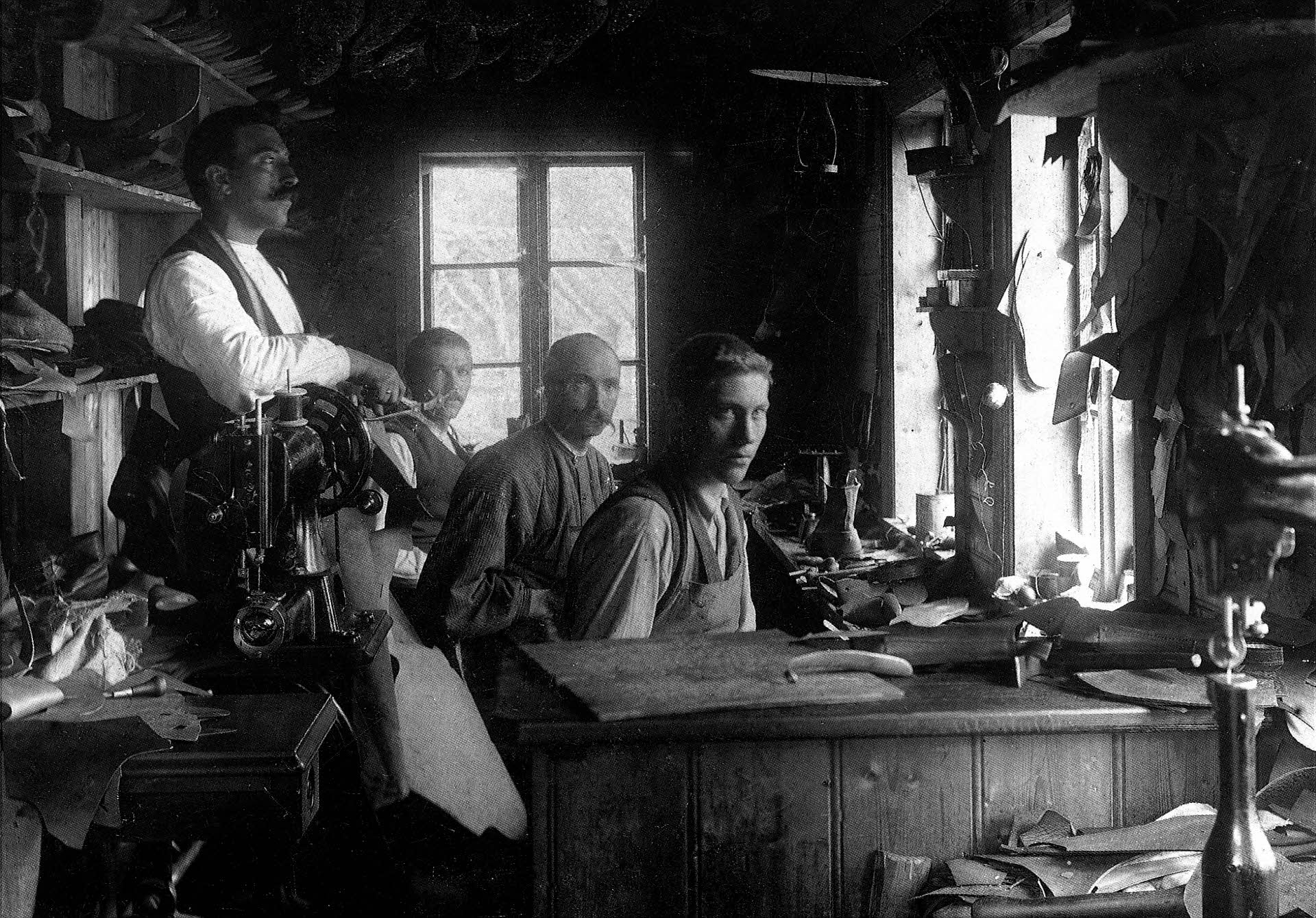 Historic photo of four men with moustache and serious faces in the 1930's sitting and working in the Aurland Shoe Factory.