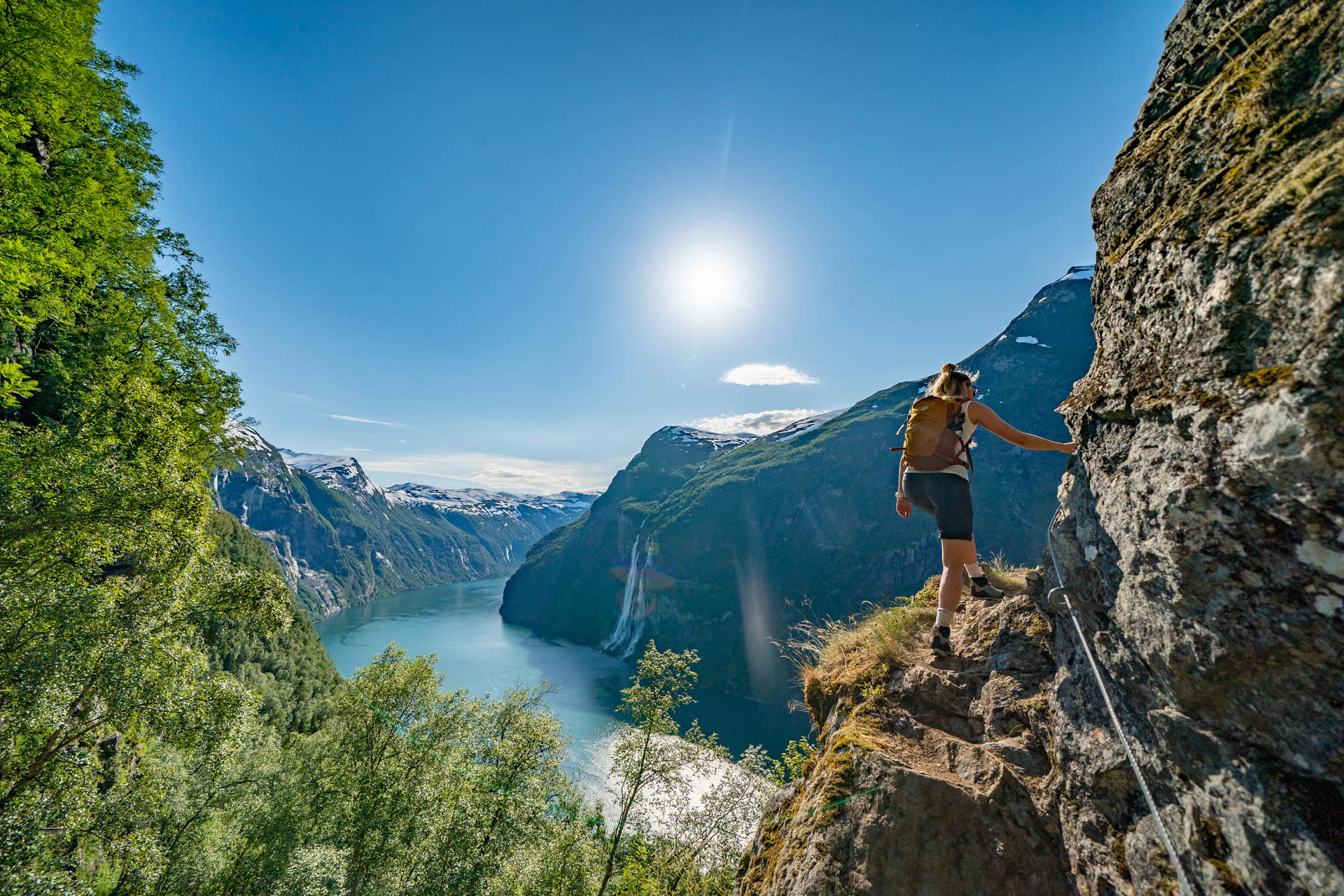 A woman hiking on a cliff with views to Geirangerfjord and waterfalls