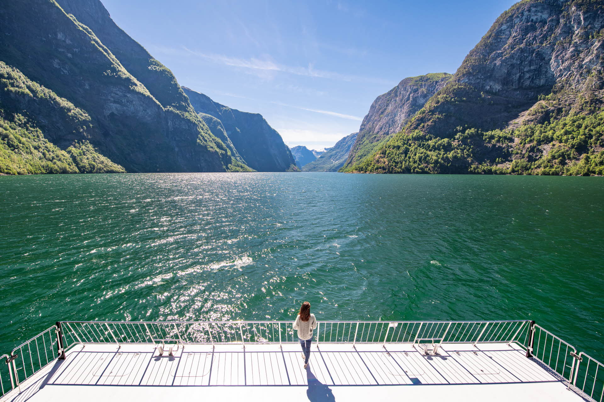 A woman stands at the bow of the Future of the Fjords, looking in towards the Nærøyfjord