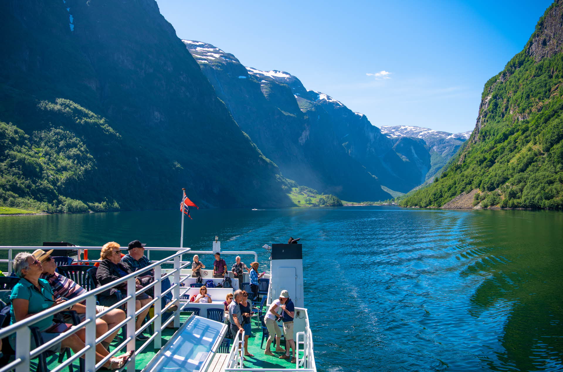阳光明媚的日子里，游客们在纳柔依峡湾 (Nærøyfjord) 的渡轮甲板上，或坐或站