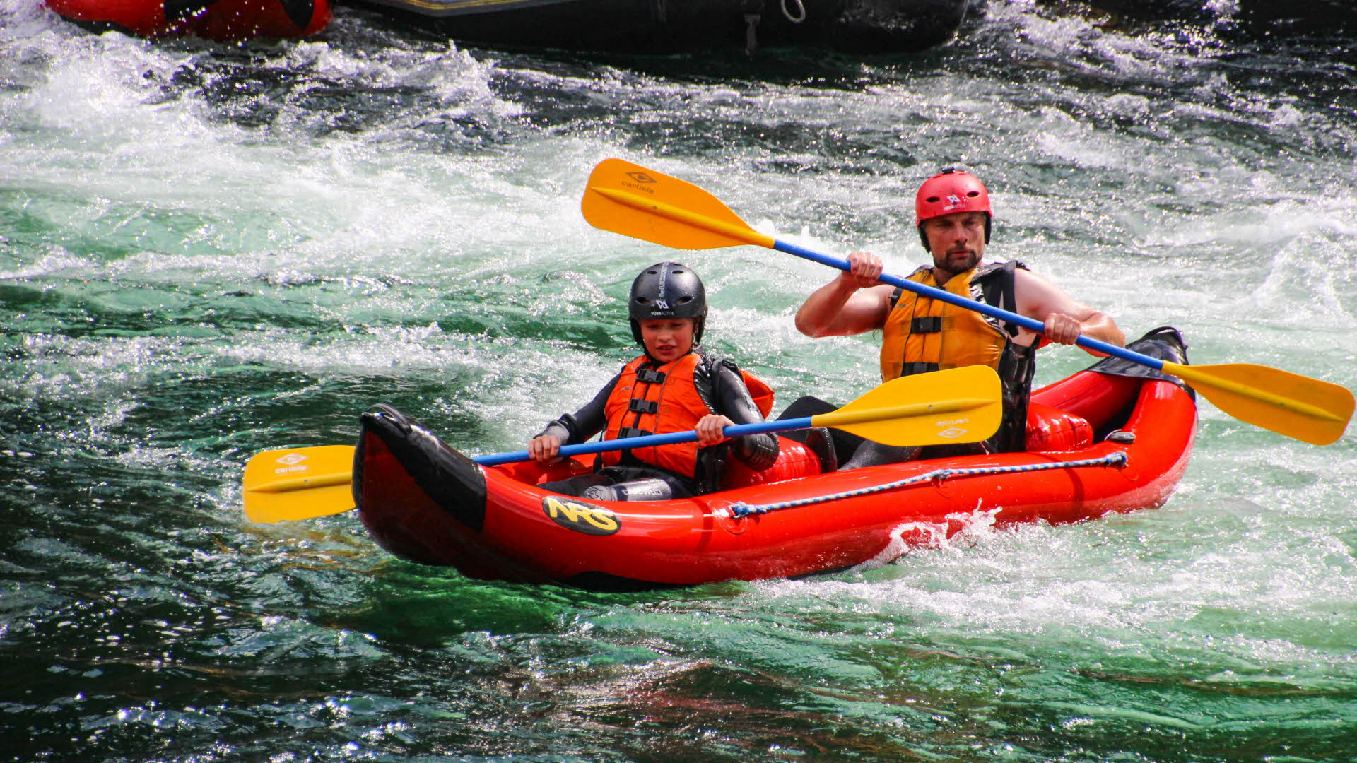 Un enfant et un adulte descendent un rapide de la rivière Vosso dans un petit raft rouge