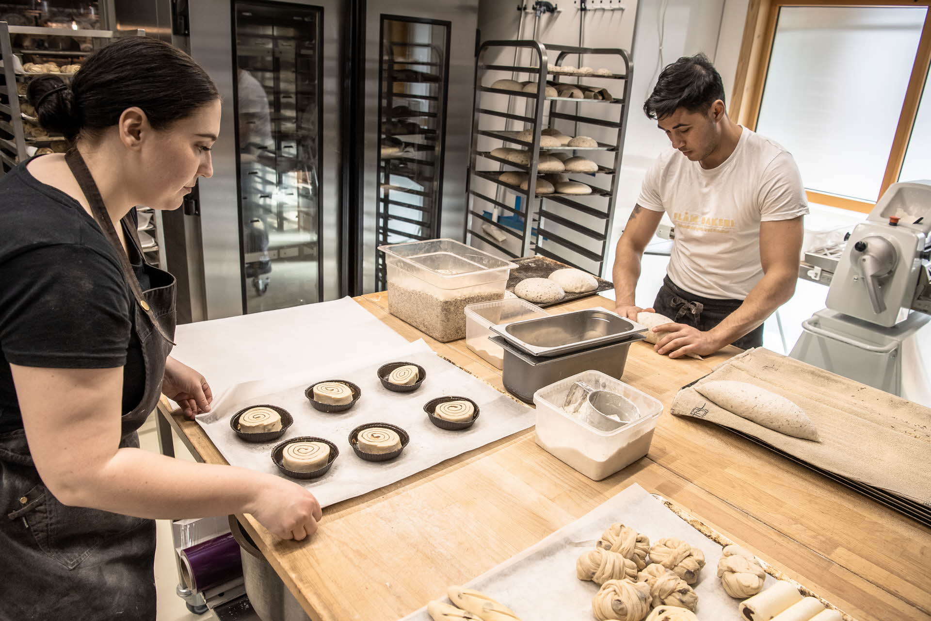 两个面包师在弗洛姆面包房 (Flåm bakery) 工作，制作面包和馅饼。
