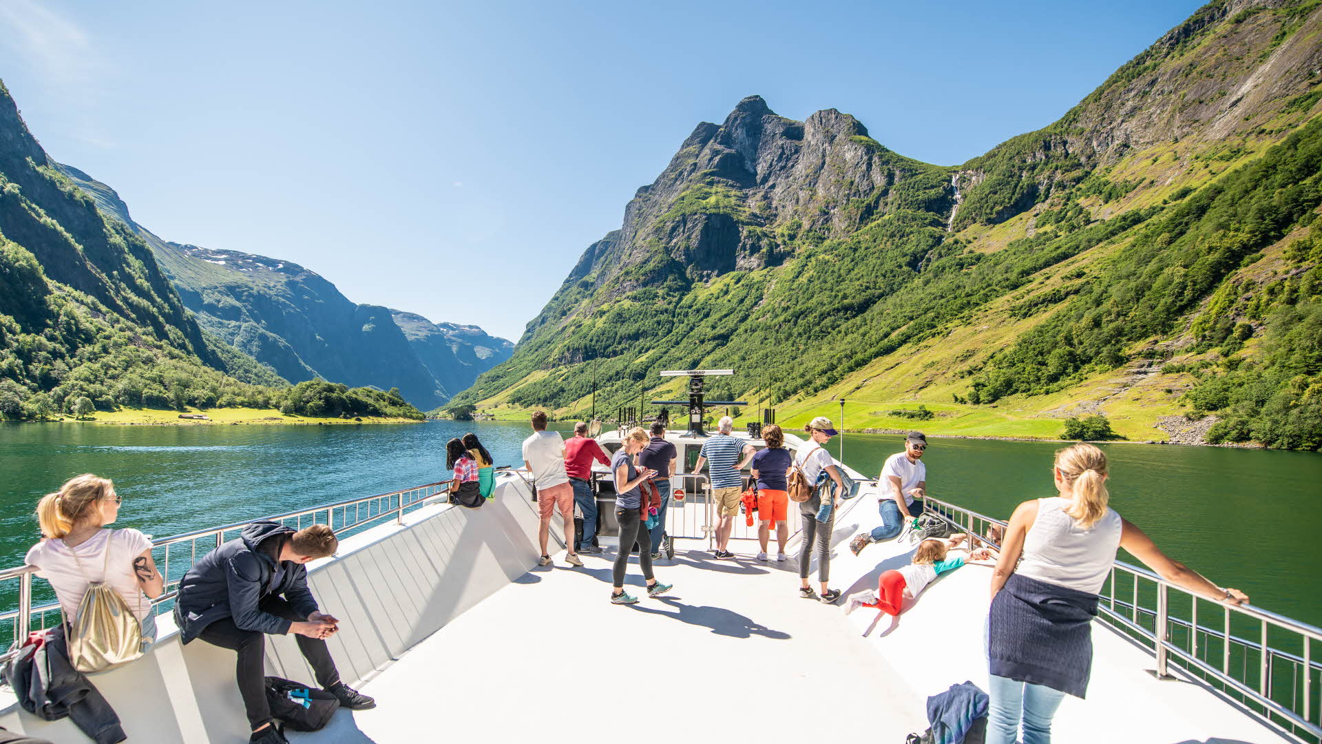 Personas disfrutando de las vistas desde la cubierta superior del Future of The Fjords un día soleado mientras navegan por el espectacular Nærøyfjord