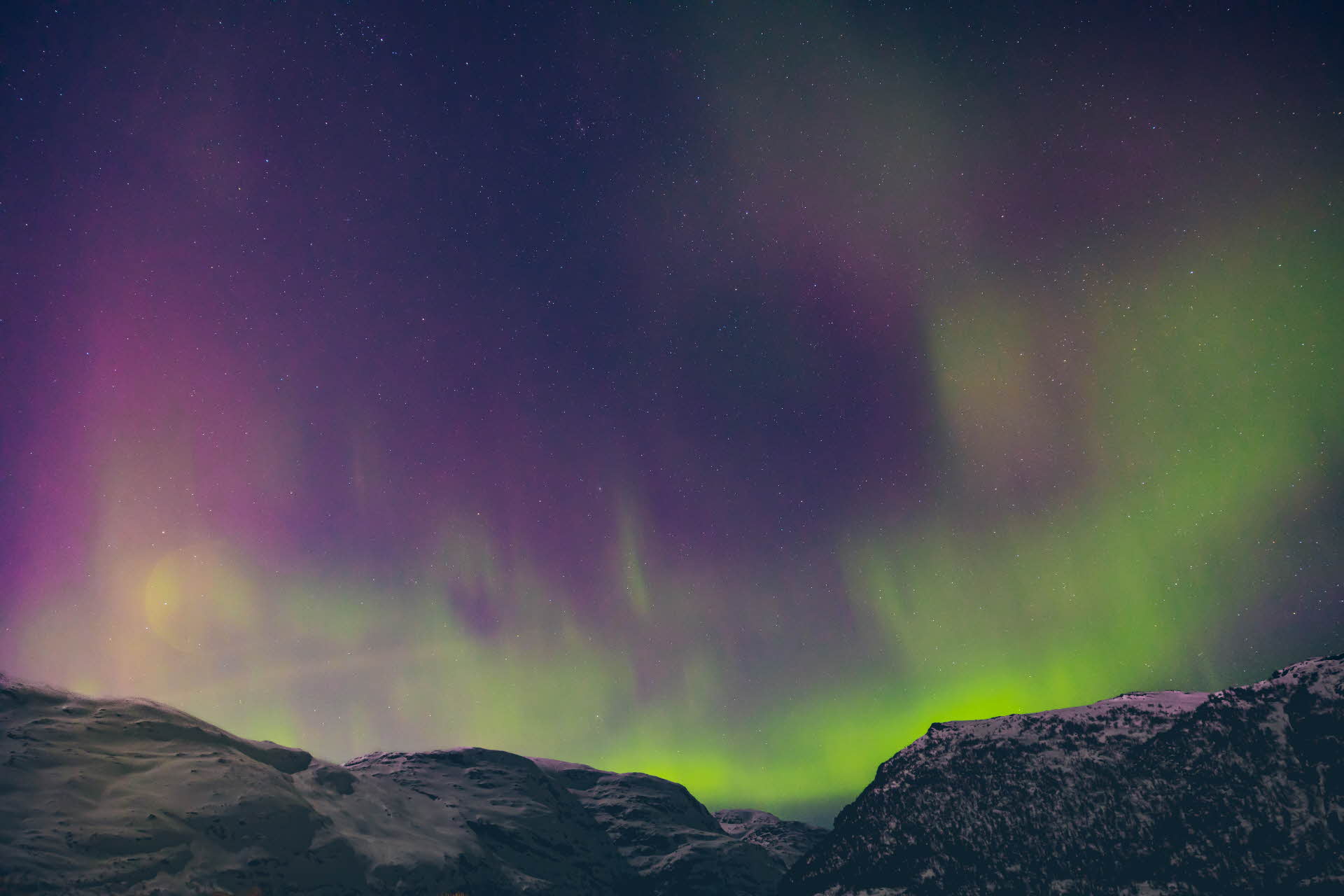 Green and purple northern lights above snowy mountain tops.