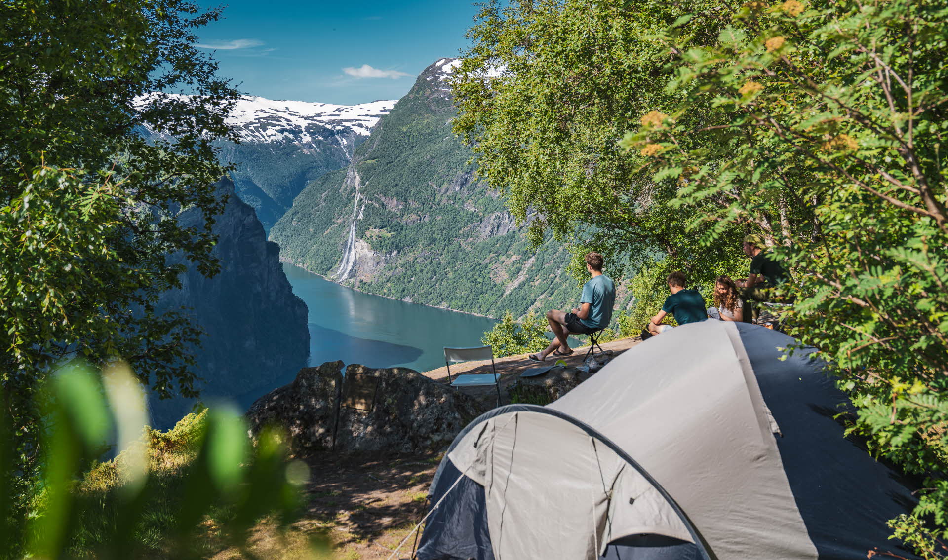 A tent and four campers on a cliff above Geirangerfjord