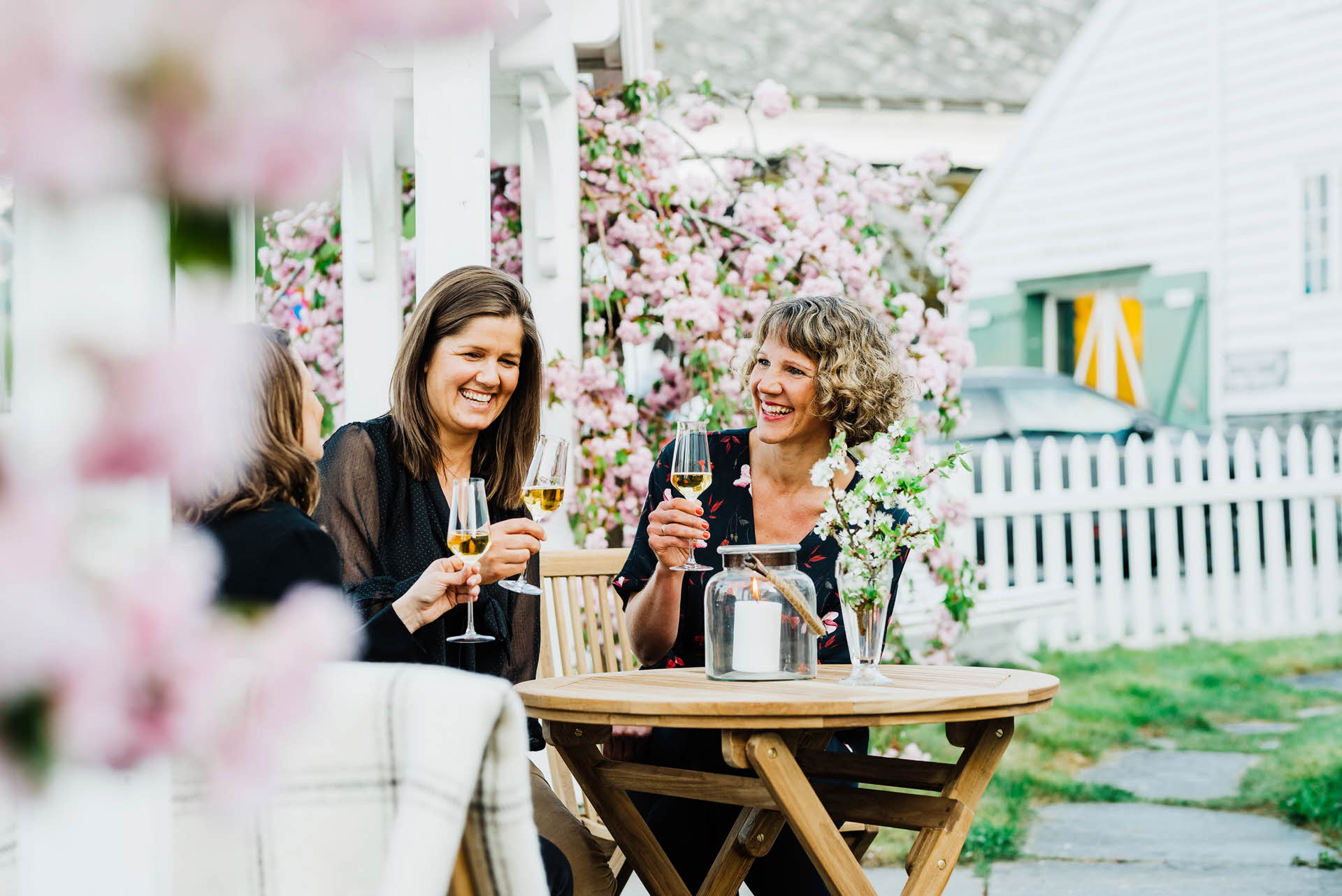 Trois femmes assises dans un jardin boivent du cidre Hardanger parmi les arbres fruitiers en fleurs