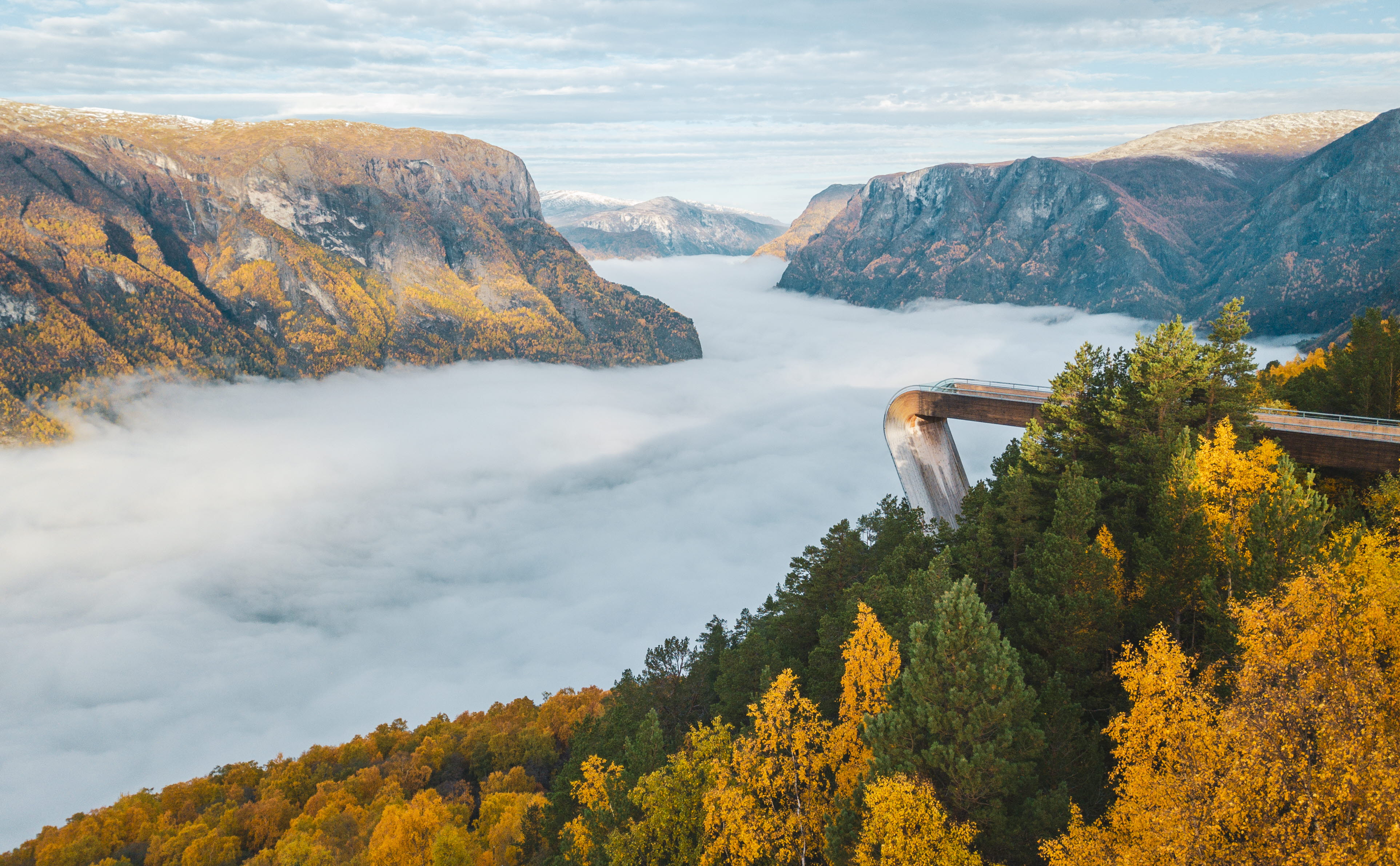 Plateforme d’observation du Stegastein surplombant l’Aurlandsfjord recouvert de brume et bordée de forêts jaunes et vertes.