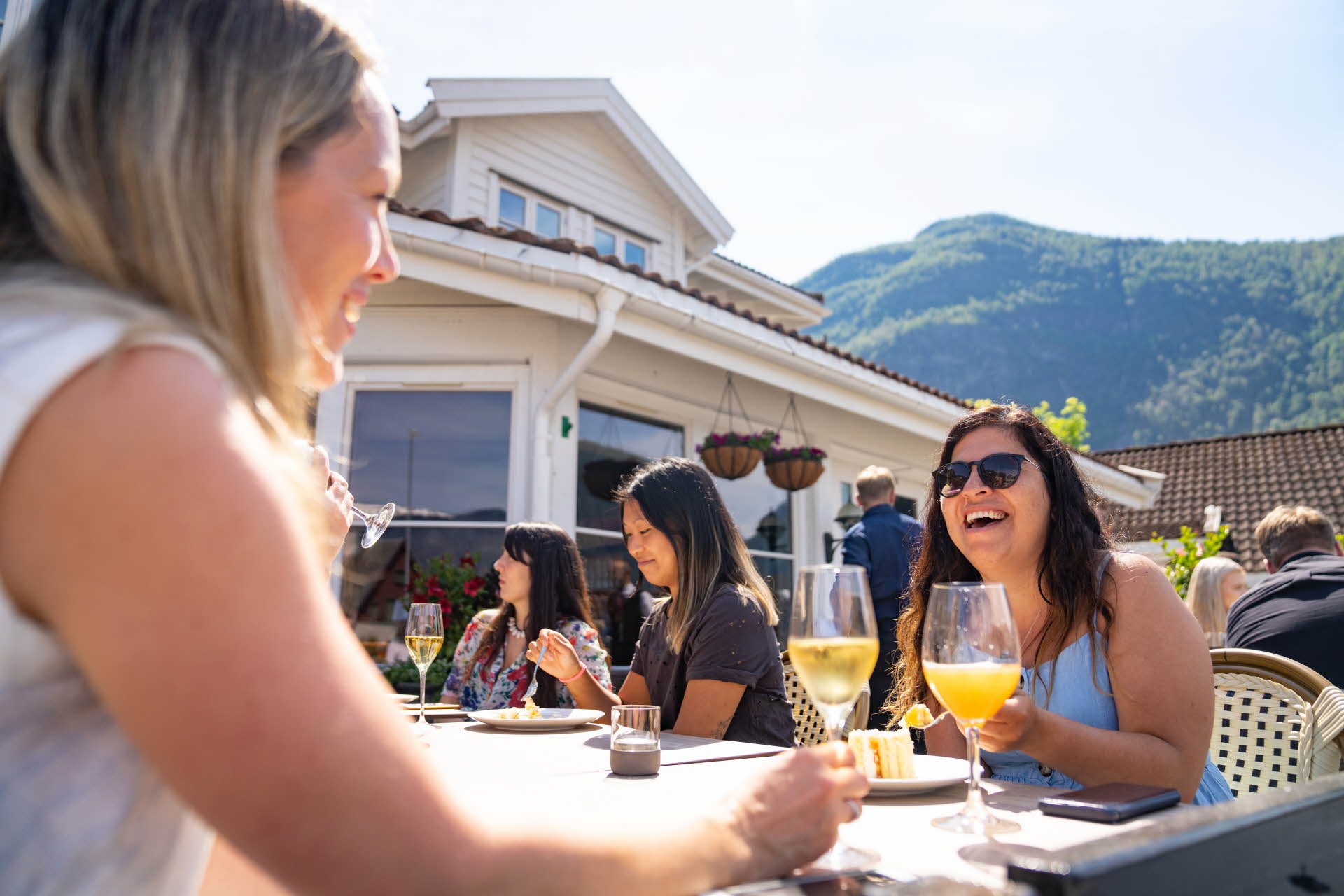 女人们坐在艾于兰峡湾酒店 (Hotel Aurlandsfjord) 外的一张桌子旁谈笑，喝着苹果酒，吃着蛋糕。 
