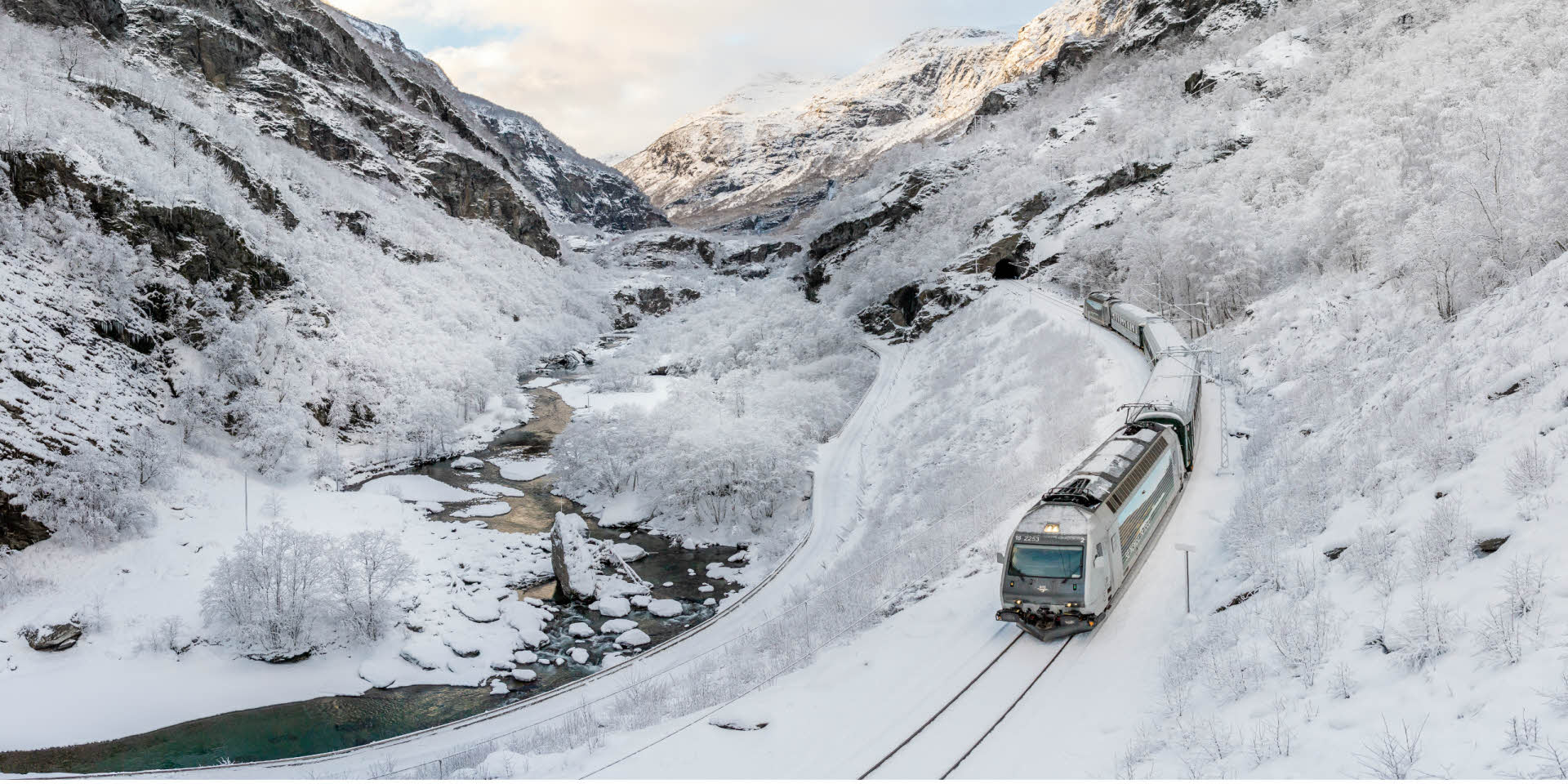 Flam 山谷的冬日景观，火车沿着蜿蜒的河流向下流驶去。
