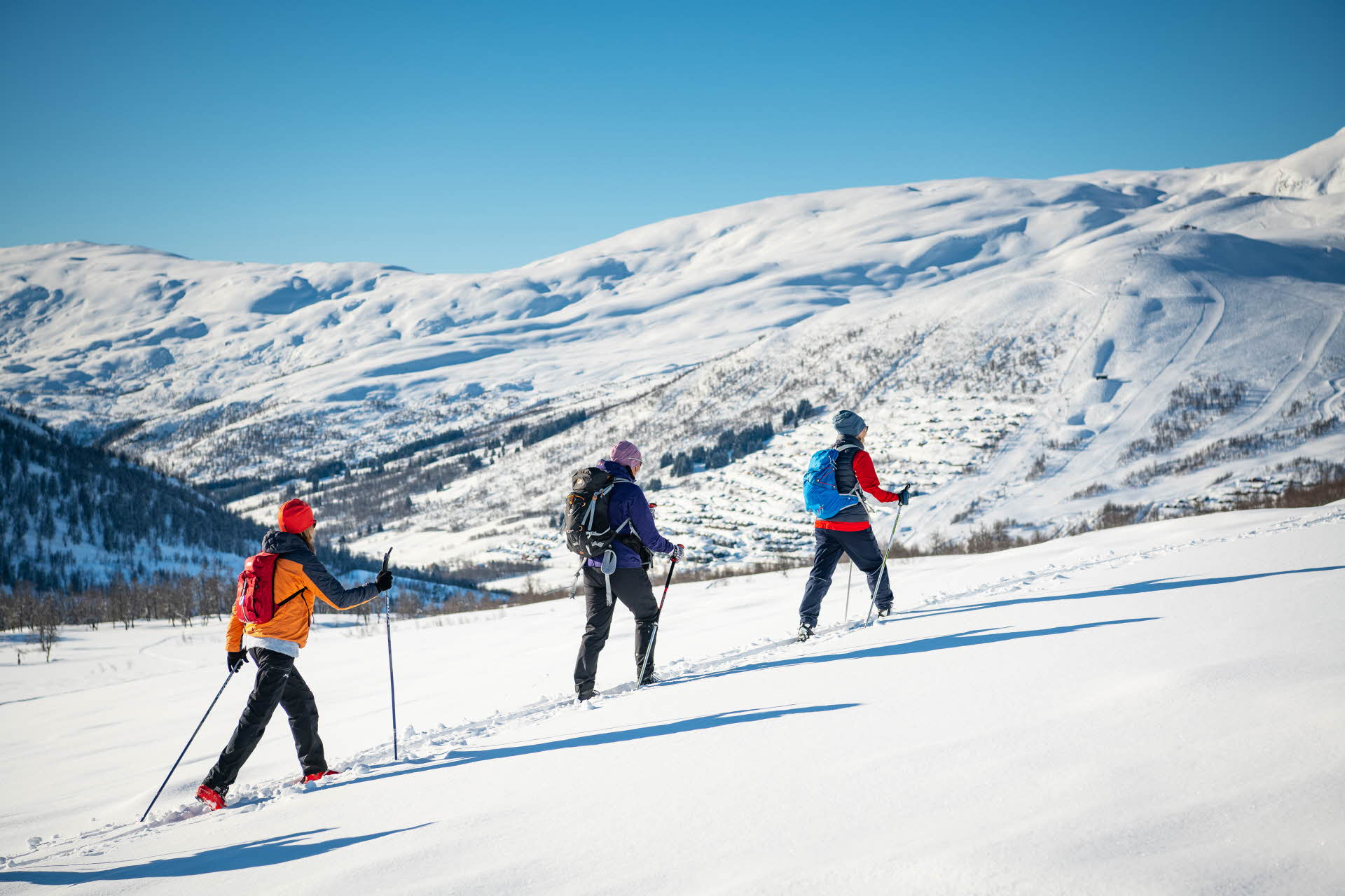 Drei Personen beim Backcountry-Skifahren in einer Reihe, mit dem Bergresort Myrkdalen im Hintergrund.