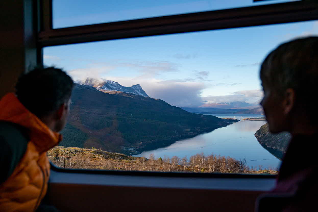 A woman and a man looking out on the fjord and mountains from The Arctic Train