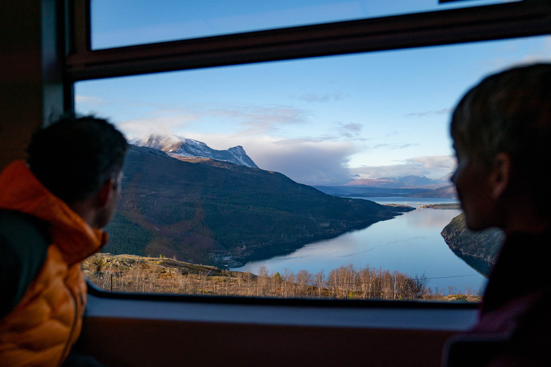 A young couple looking out of the carriage window on the Arctic Train as it passes a viewpoint overlooking the Rombaksfjord