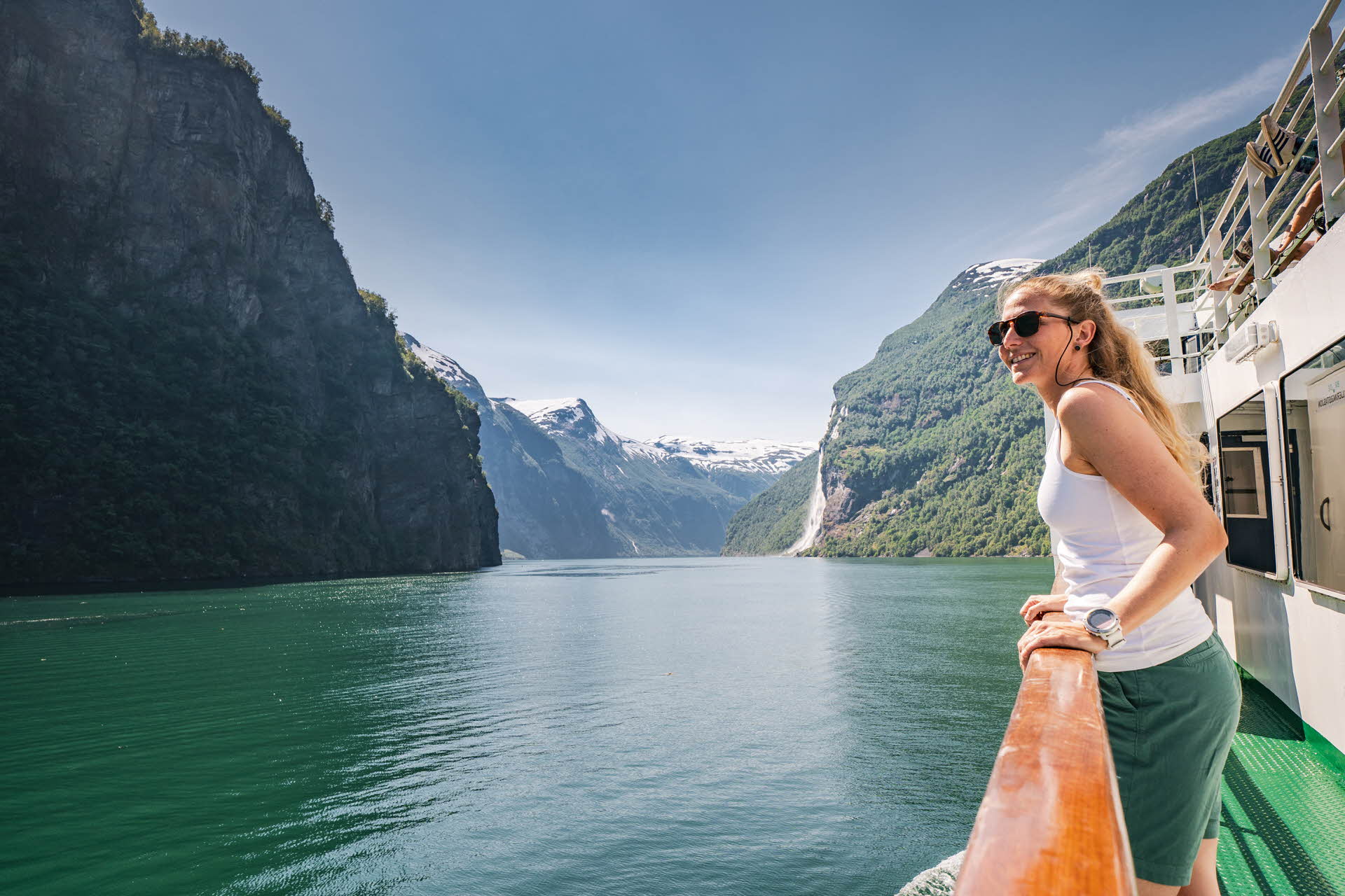 Eine lächelnde Frau steht an Deck einer Fähre auf dem Geirangerfjord