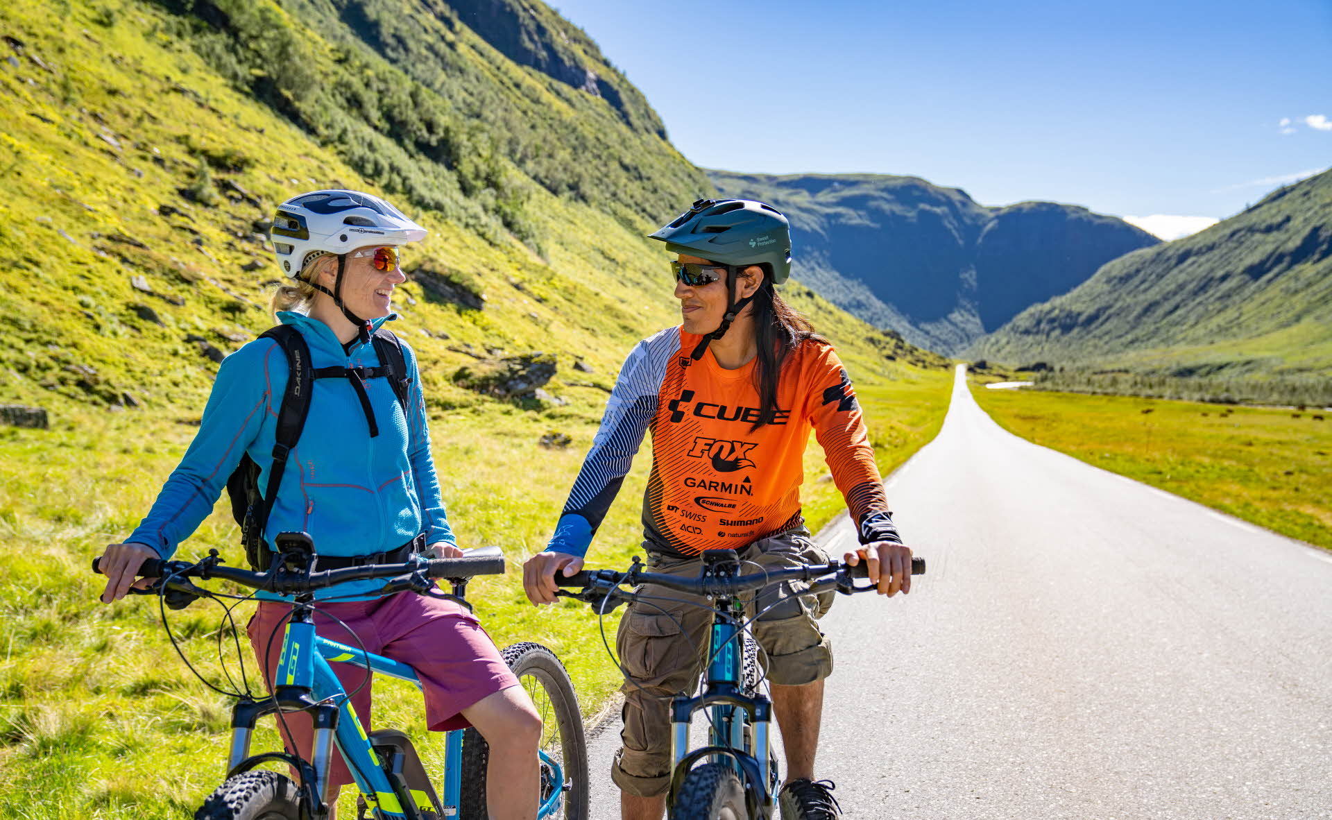 在通往维卡山 (Vikafjell) 的山区公路上，一名女士和一名男士在自行车上休息