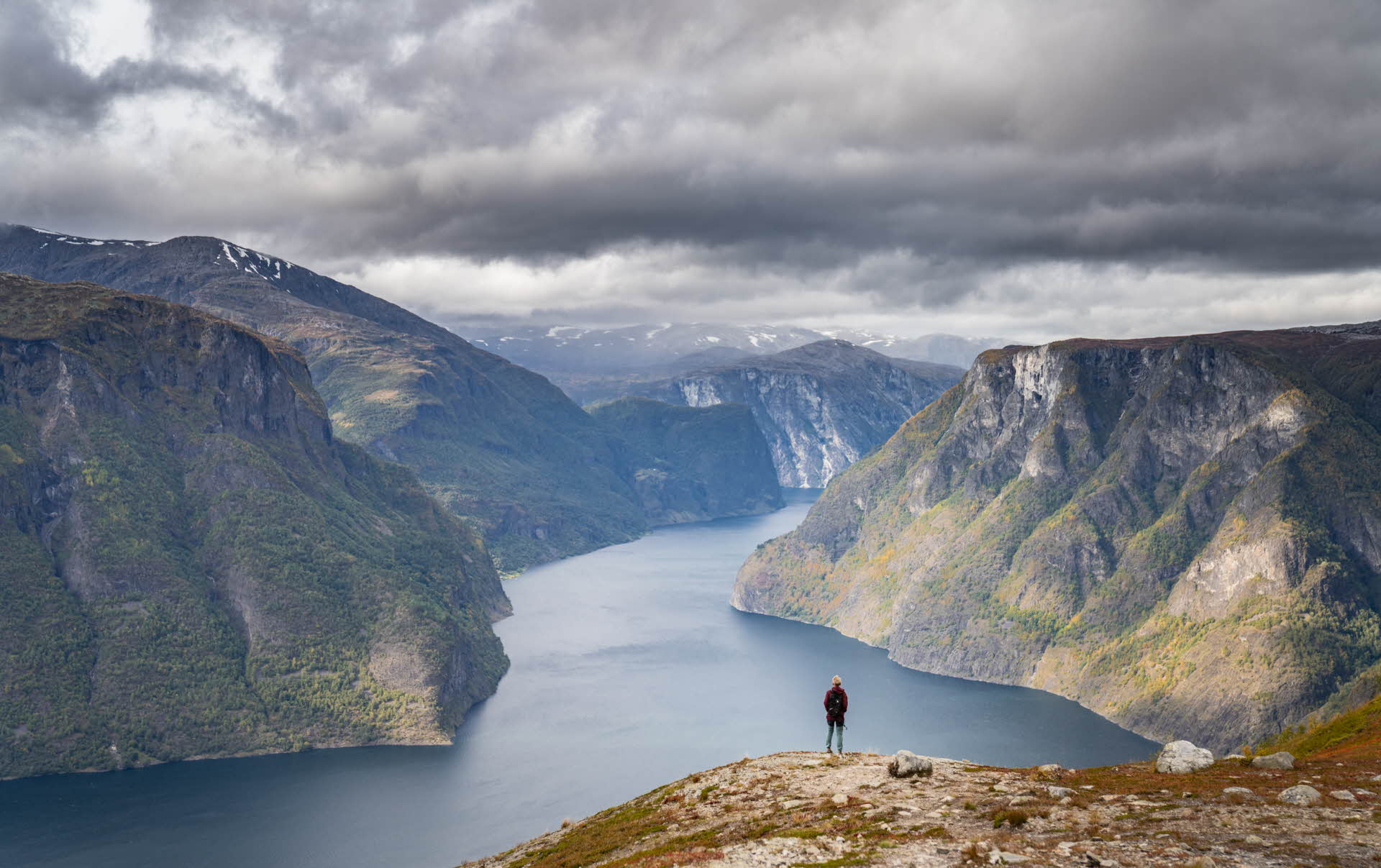 Une personne est debout sur le mont Prest et regarde l’Aurlandsfjord par une journée d’automne nuageuse.