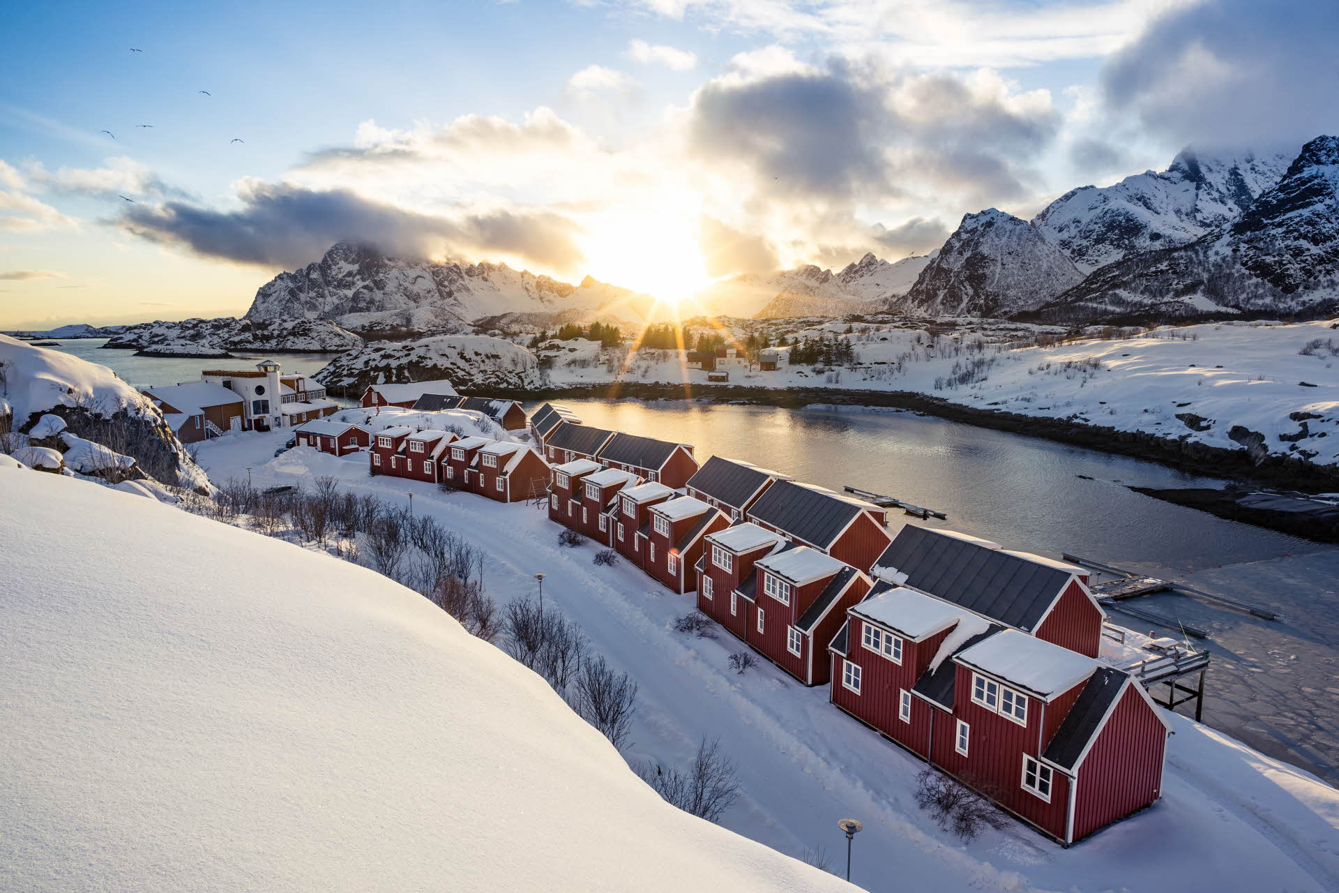 Le paysage hivernal entourant le Nyvågar Rorbuhotell. Montagnes, mer et soleil se cachant derrière les nuages.
