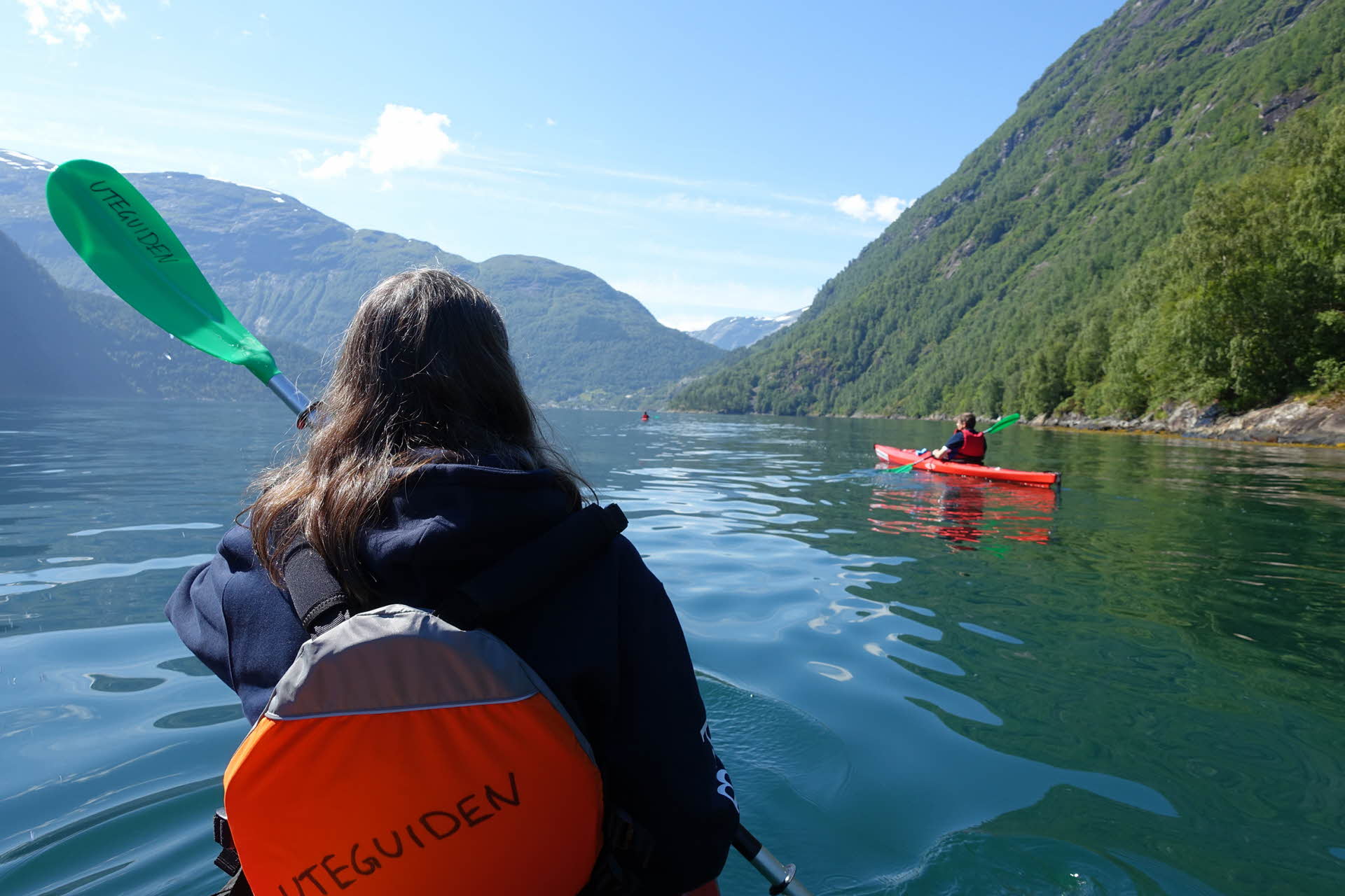 Una mujer en un kayak rojo con remos verdes junto a otro kayakista por el Geirangerfjord