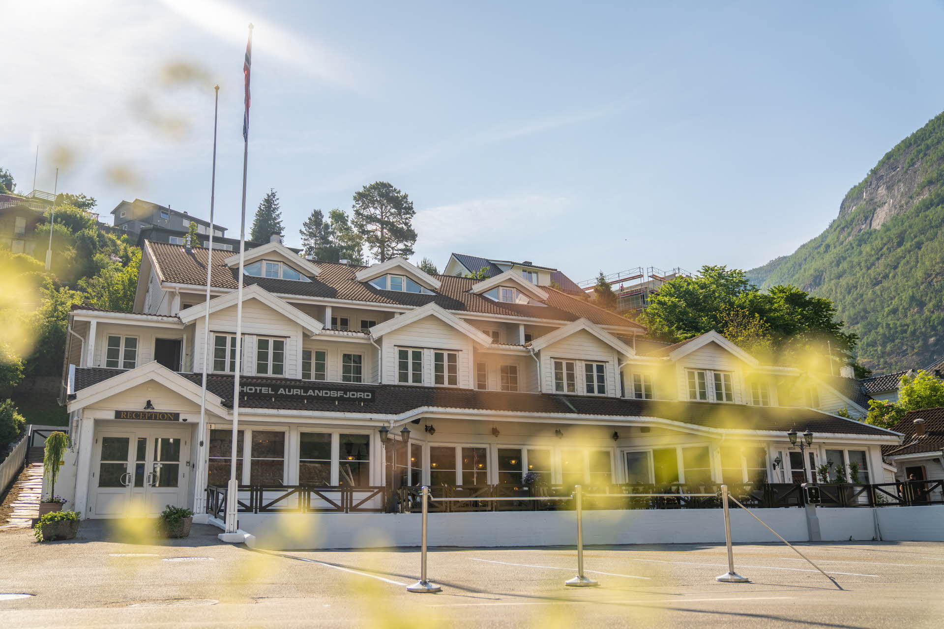 阳光明媚，艾于兰峡湾酒店 (Hotel Aurlandsfjord) 的外立面，前景里是绿叶