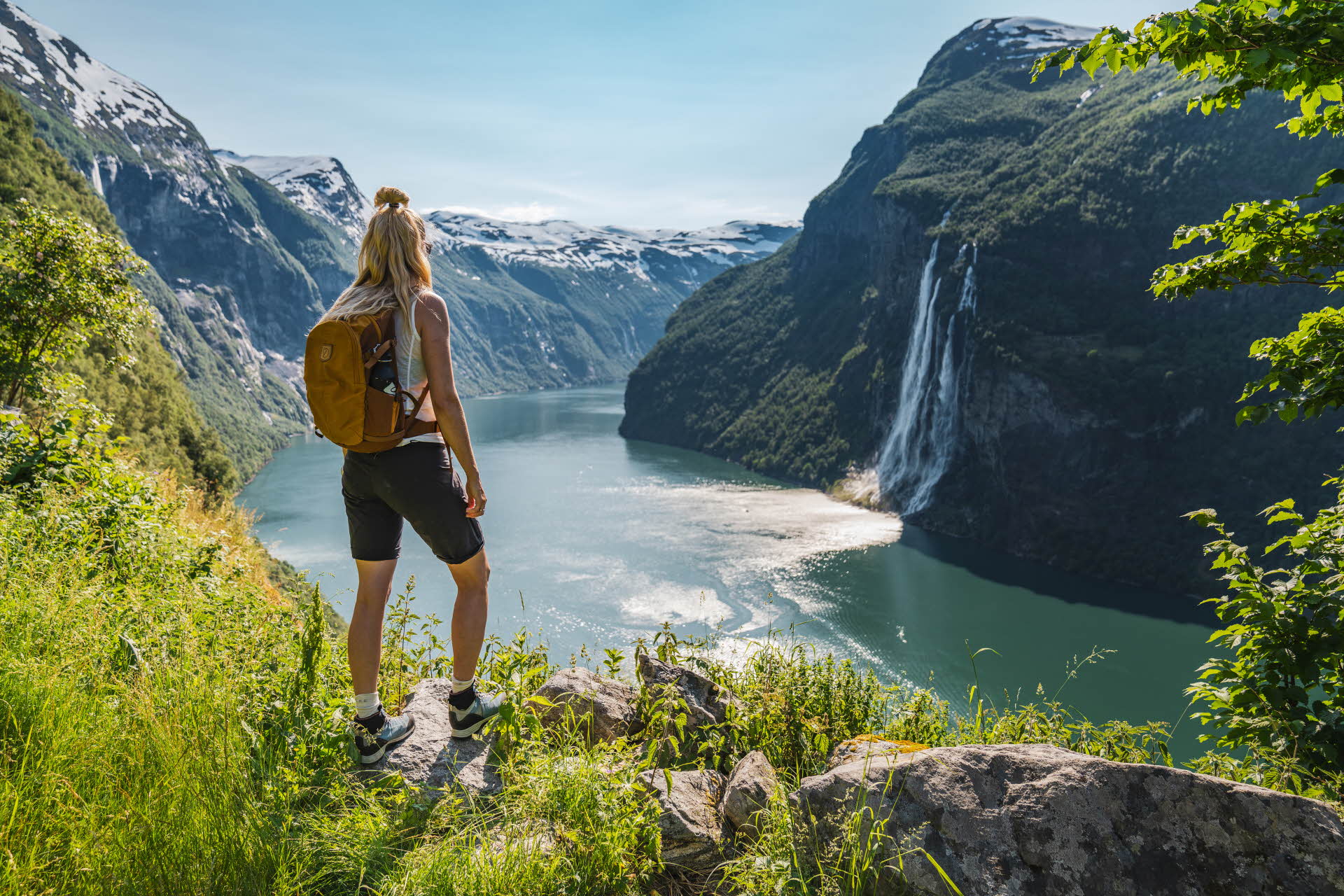 Una mujer sobre una roca mirando hacia la cascada de las Siete Hermanas y al Geirangerfjord