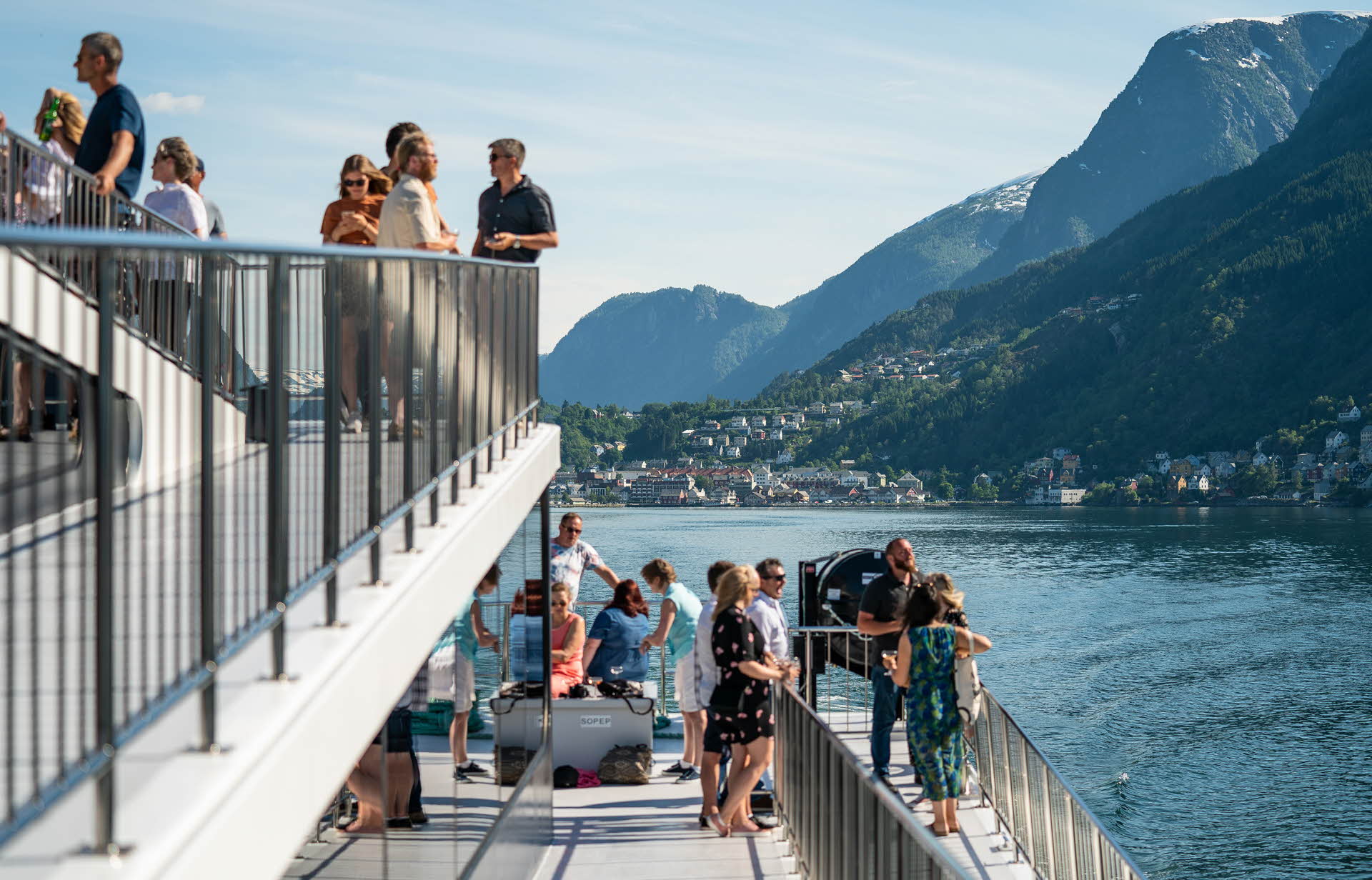 People on the deck of a catamaran on the Hardangerfjord with Odda in the background