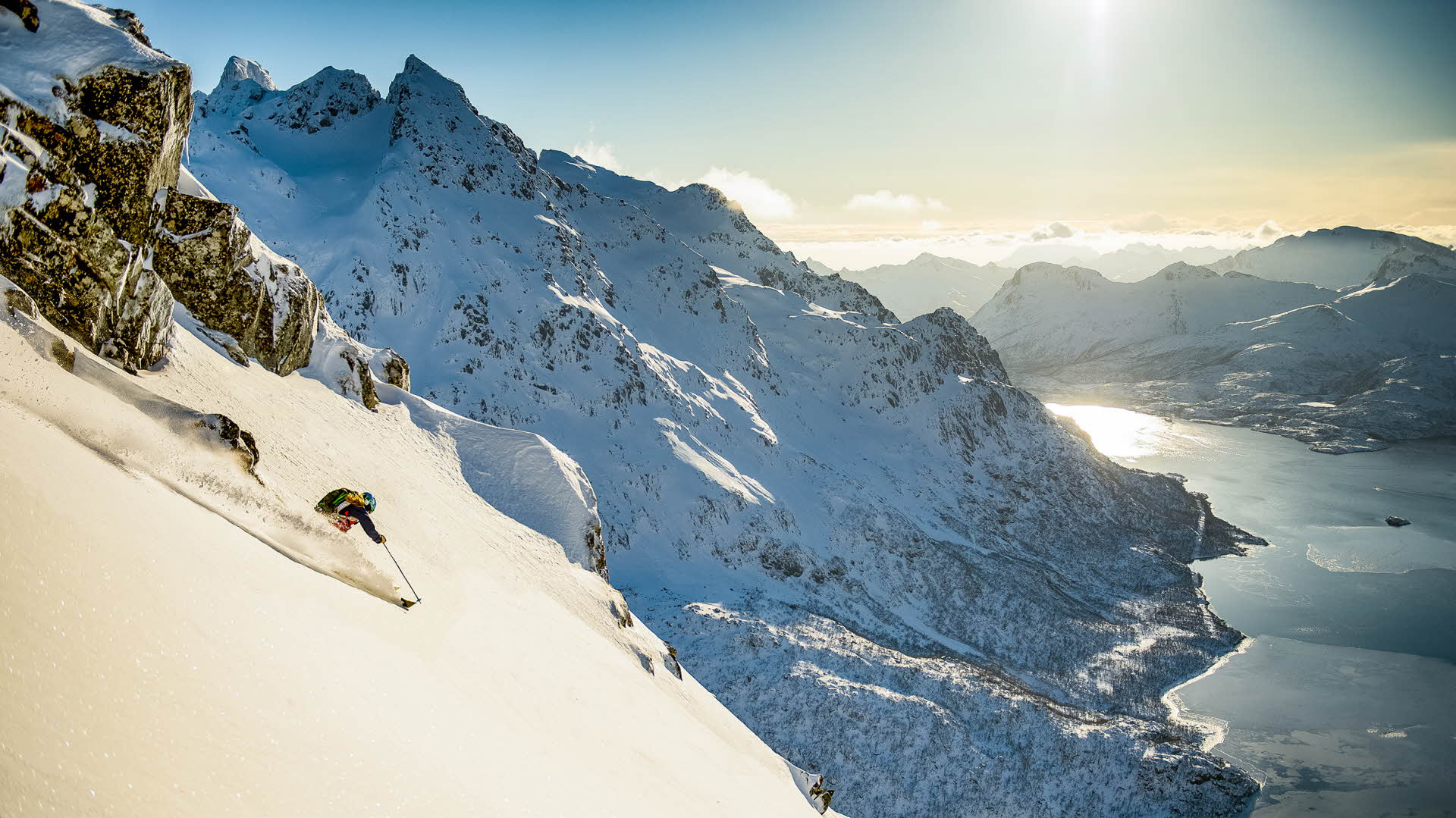 A person skiing down a mountain in fresh snow. Sea below and mountain ranges surrounding.