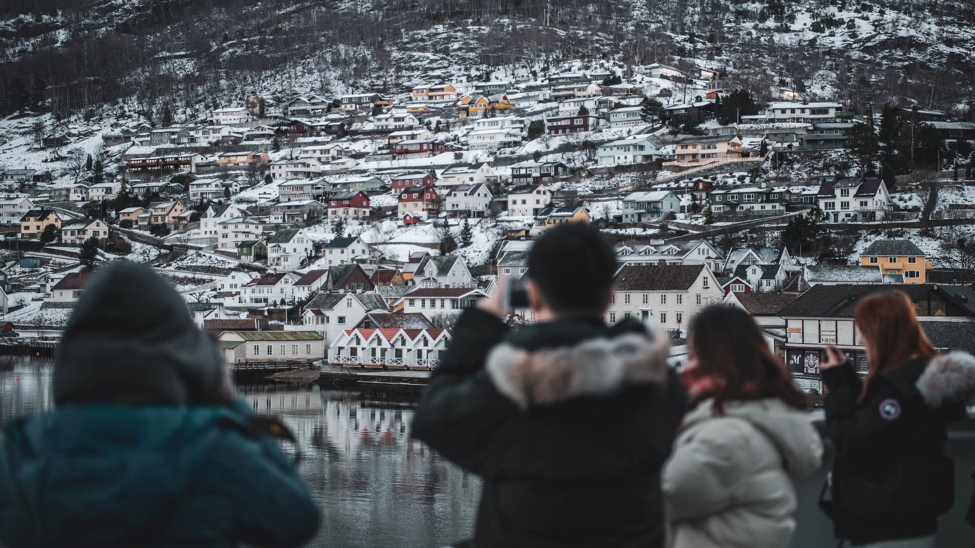 A tourist standing on a boat photographing Aurland village centre in the winter