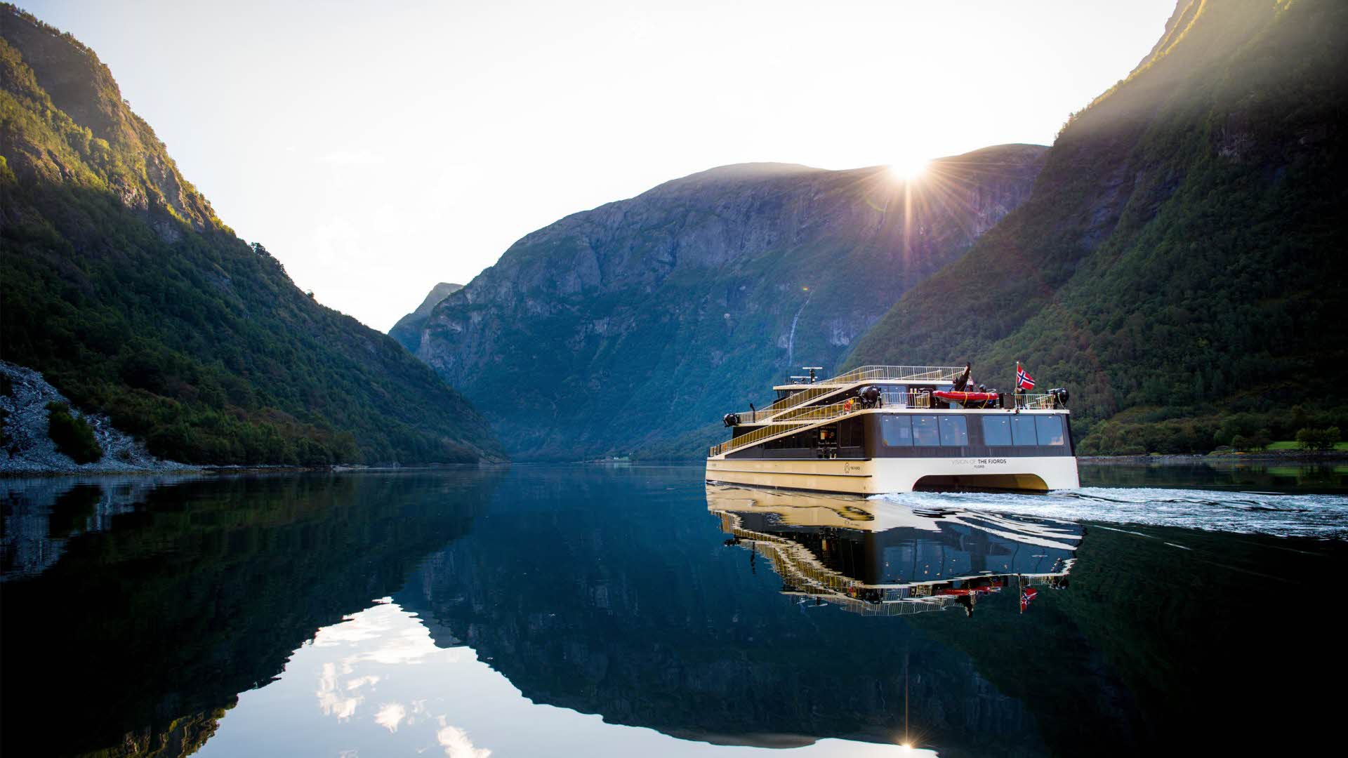 An electric boat sails across the Aurlandsfjord at dusk