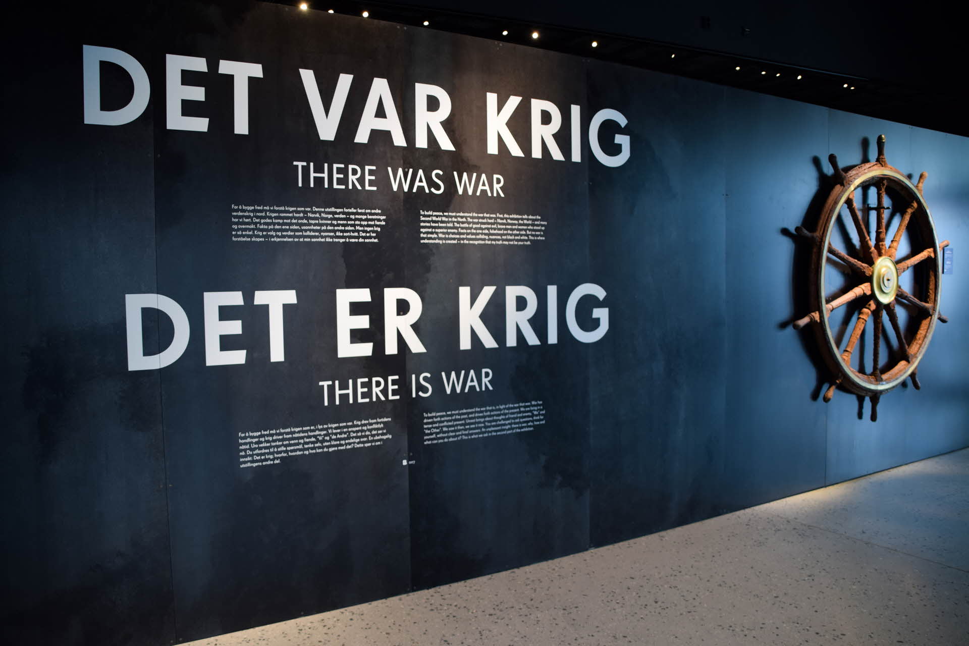 Wand mit Text über den Krieg und einem Steuerrad im Kriegsmuseum Narvik.