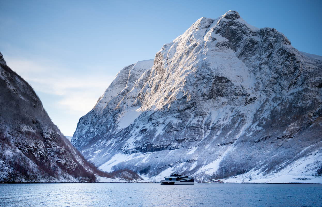 Ein Passagierkatamaran auf einem Fjord vor steilen, schneebedeckten Bergen. Blauer Himmel. Foto.
