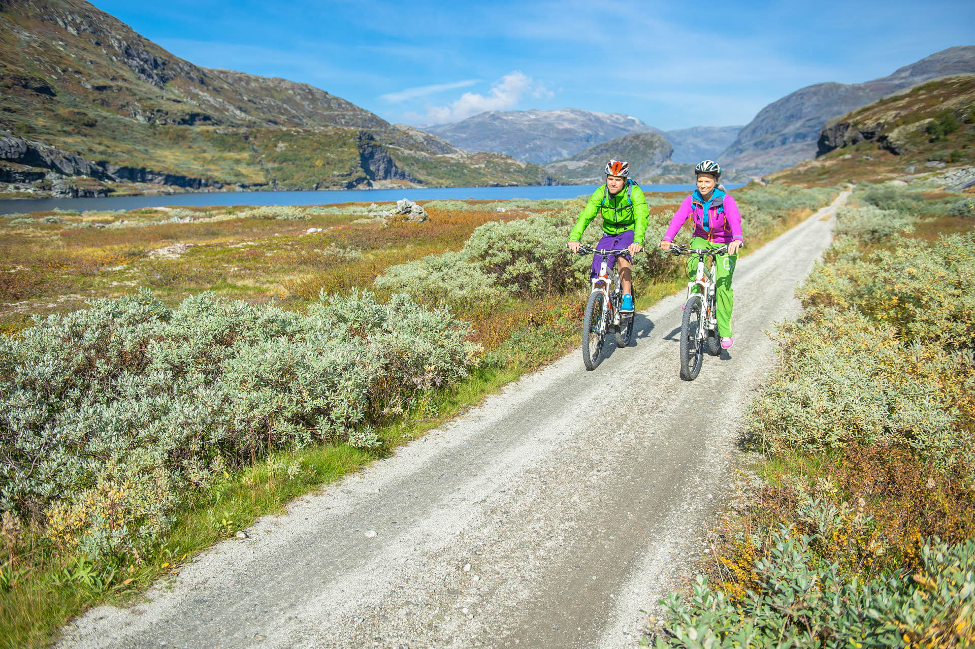 A man and a woman cycling on a montainuos gravel road in sunny weather.