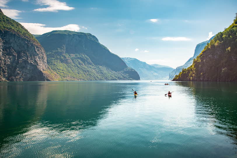 View of the Aurlandsfjord on a summer day. Three kayakers and steep, green mountains. 