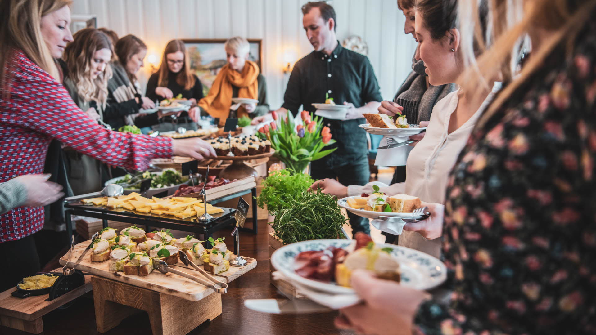 Des personnes avec des assiettes à la main, debout autour d’un buffet proposant un large choix de plats et de décorations colorées, au Fretheim Hotel.