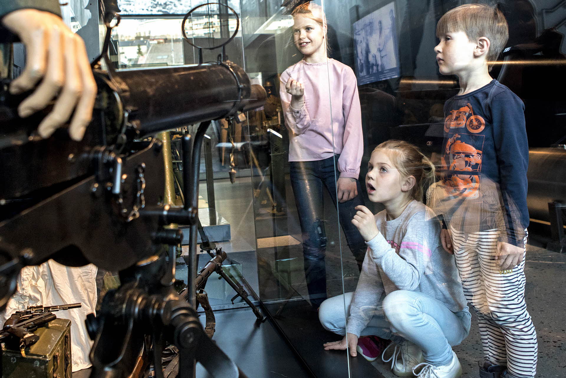 Two girls and a boy looks at a display case showing a soldier and a gun. 