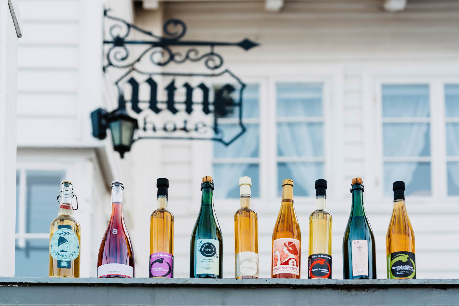 9 different shaped cider bottles lined up on top of railing outside Utne Hotel Hardanger Norway 