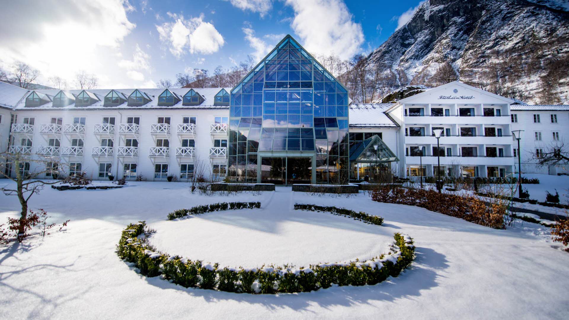 Das Hotel Fretheim vom verschneiten Garten aus gesehen, blauer Himmel und kleine Wolken im Hintergrund. 