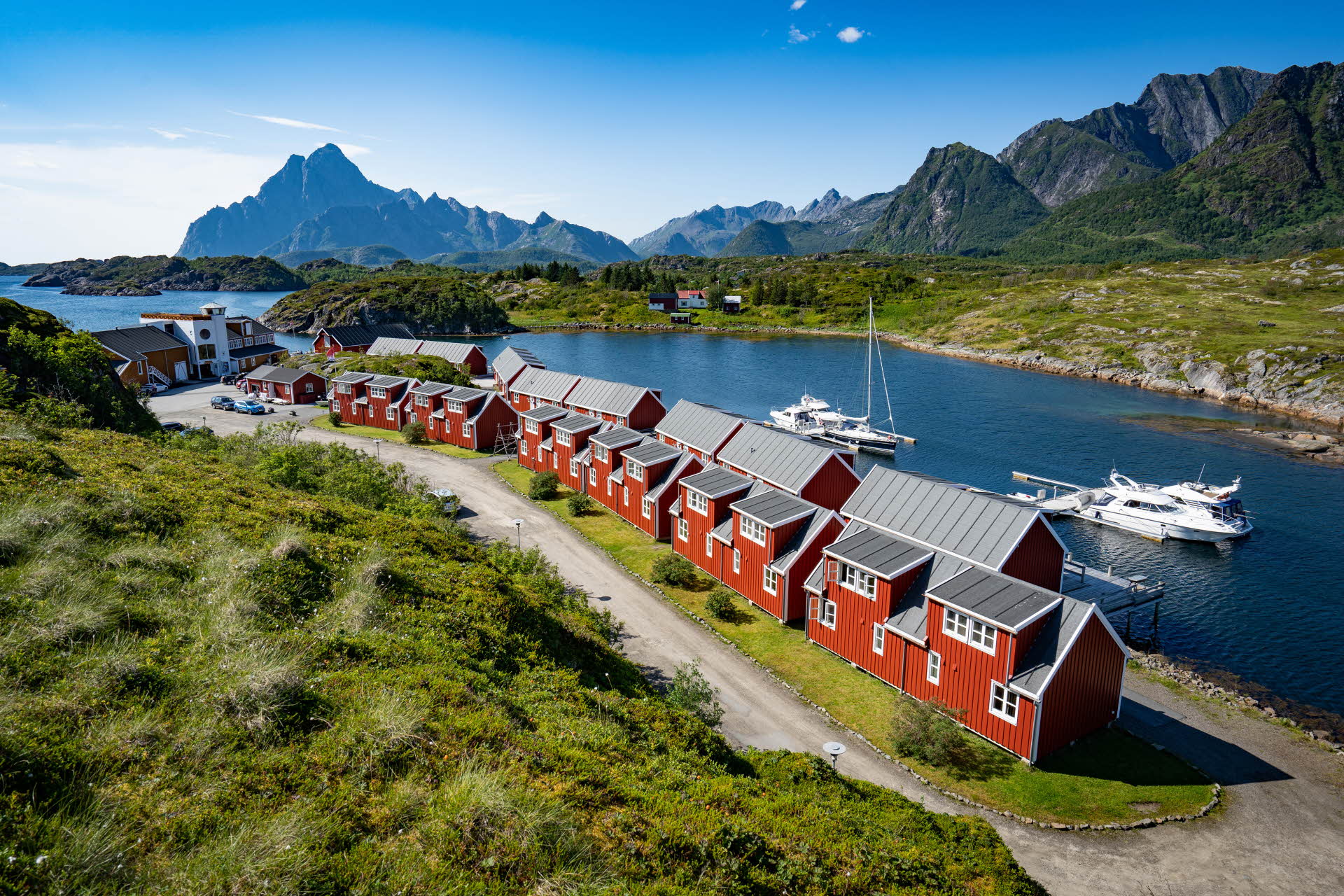 Les petites cabanes rouges du Nyvågar Rorbuhotell en bord de mer, avec des montagnes à l’horizon.