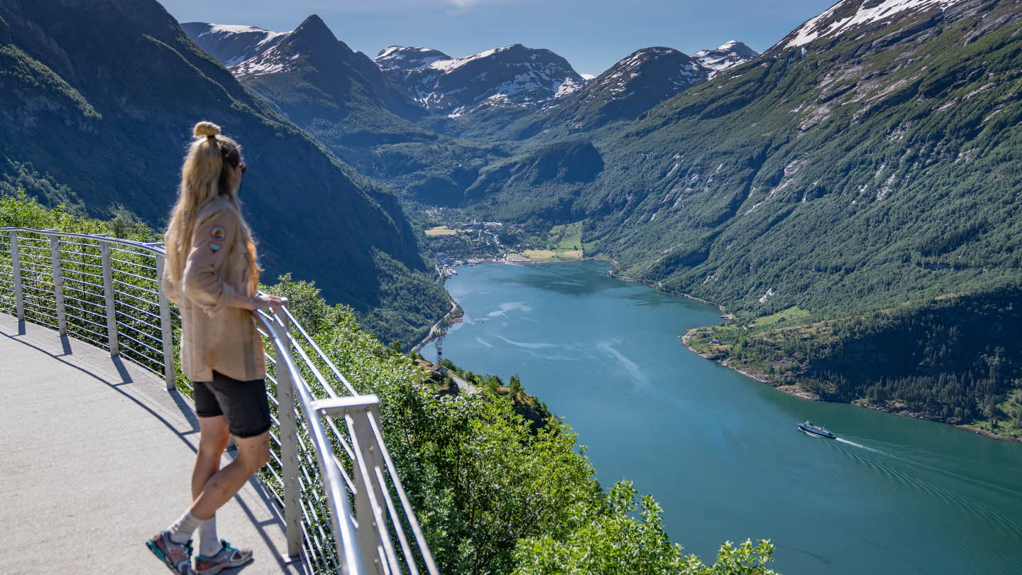 A woman stands on Ørnesvingen viewing platform looking towards Geiranger